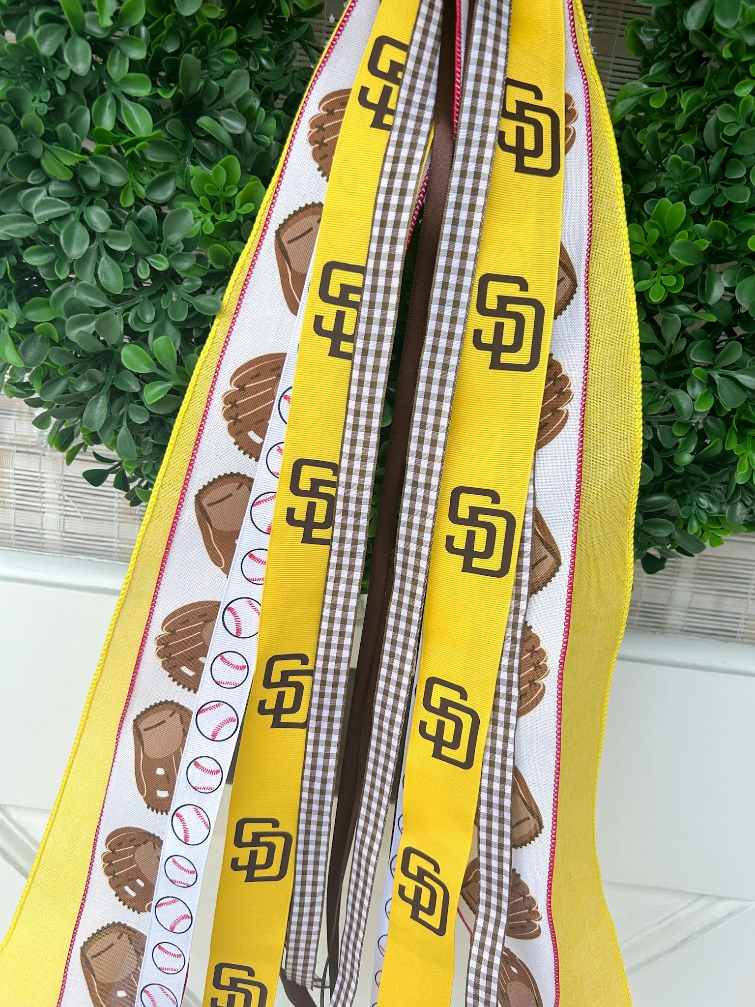 Various San Diego Padres-themed ribbons and fabric ribbons with baseball and baseball glove patterns, hanging on green wreath.