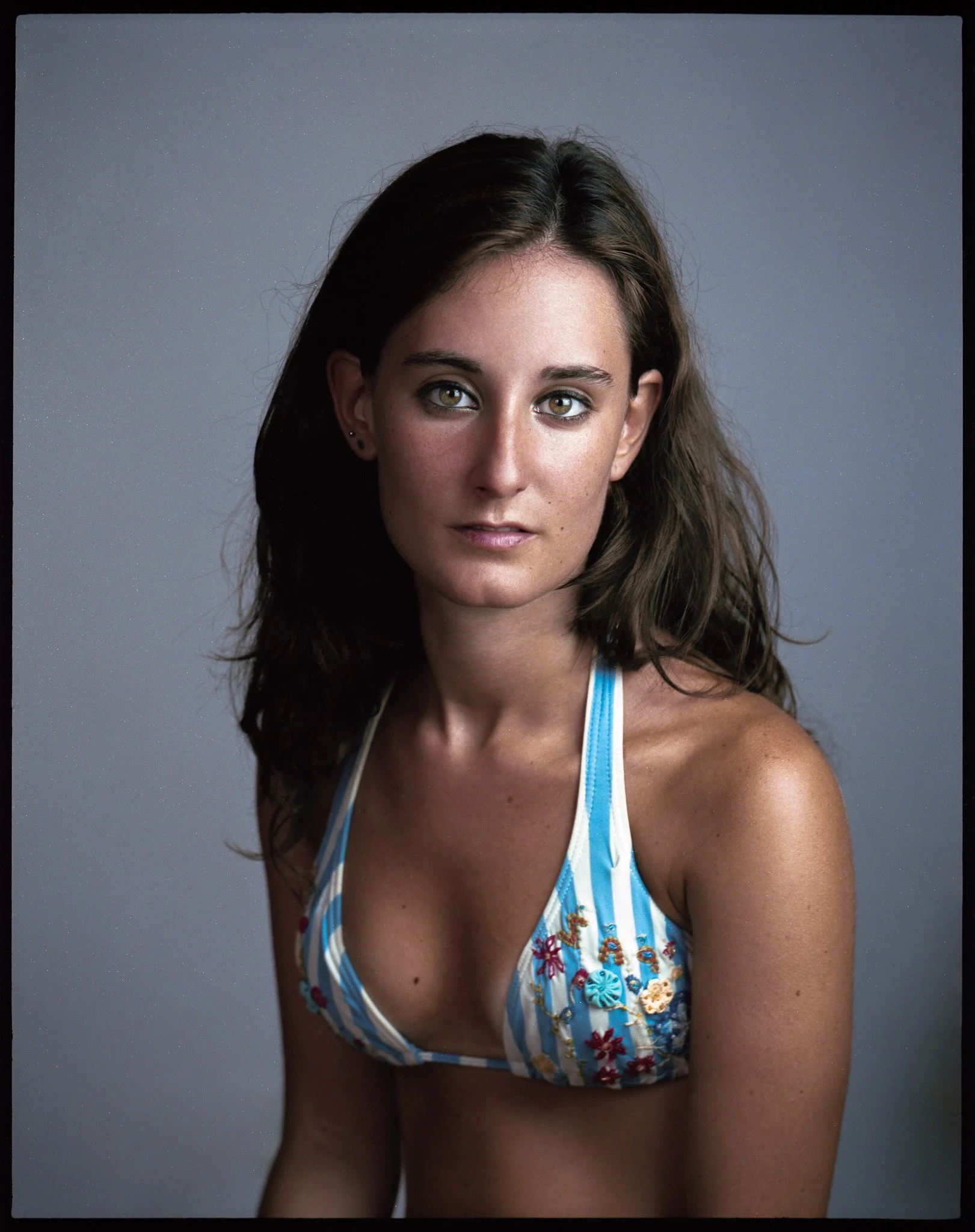 A woman with long brown hair wearing a blue and white striped bikini top with embroidered floral details.