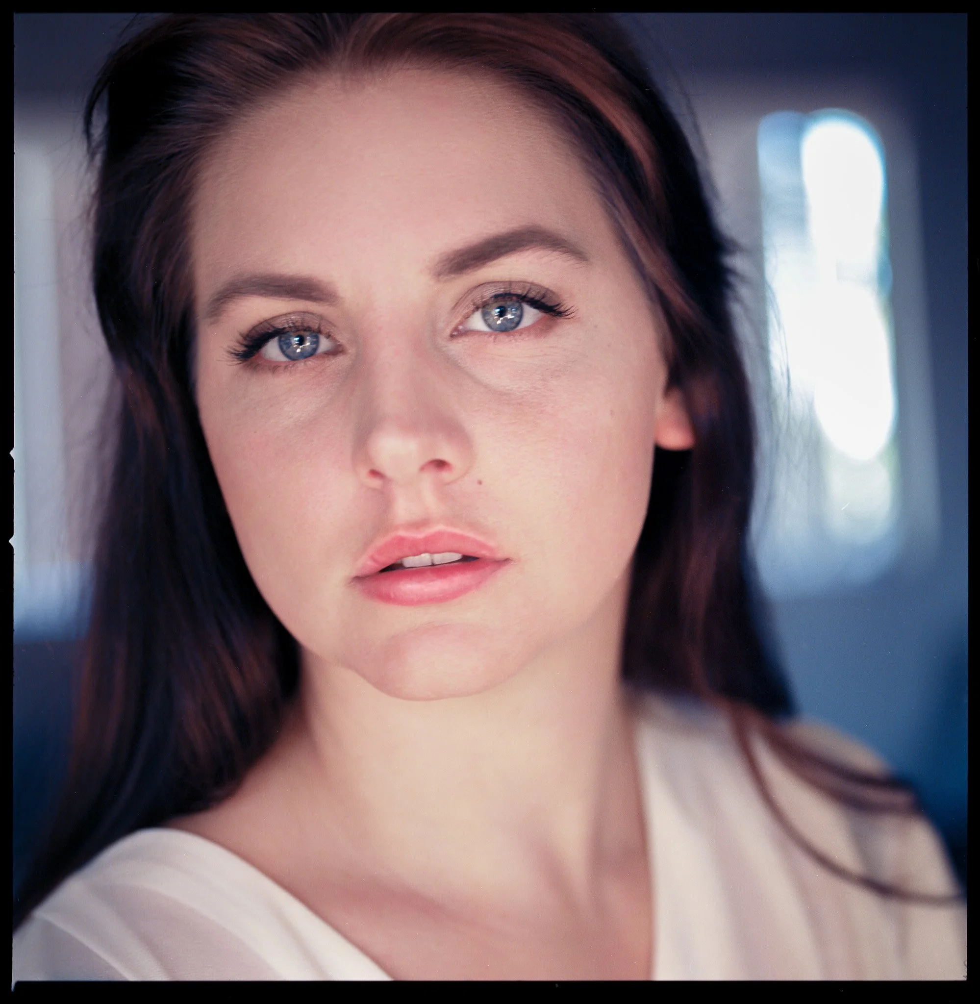 Close-up of a woman with long dark hair, blue eyes, and light makeup, looking directly at the camera.