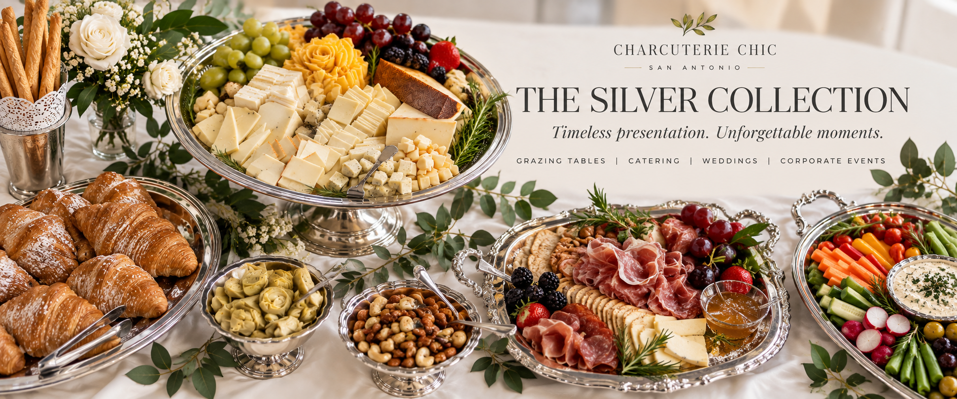 The Silver Collection luxury grazing table with artisan cheeses, cured meats, croissants, fresh fruit and vegetables displayed on elegant vintage silver serving pieces.