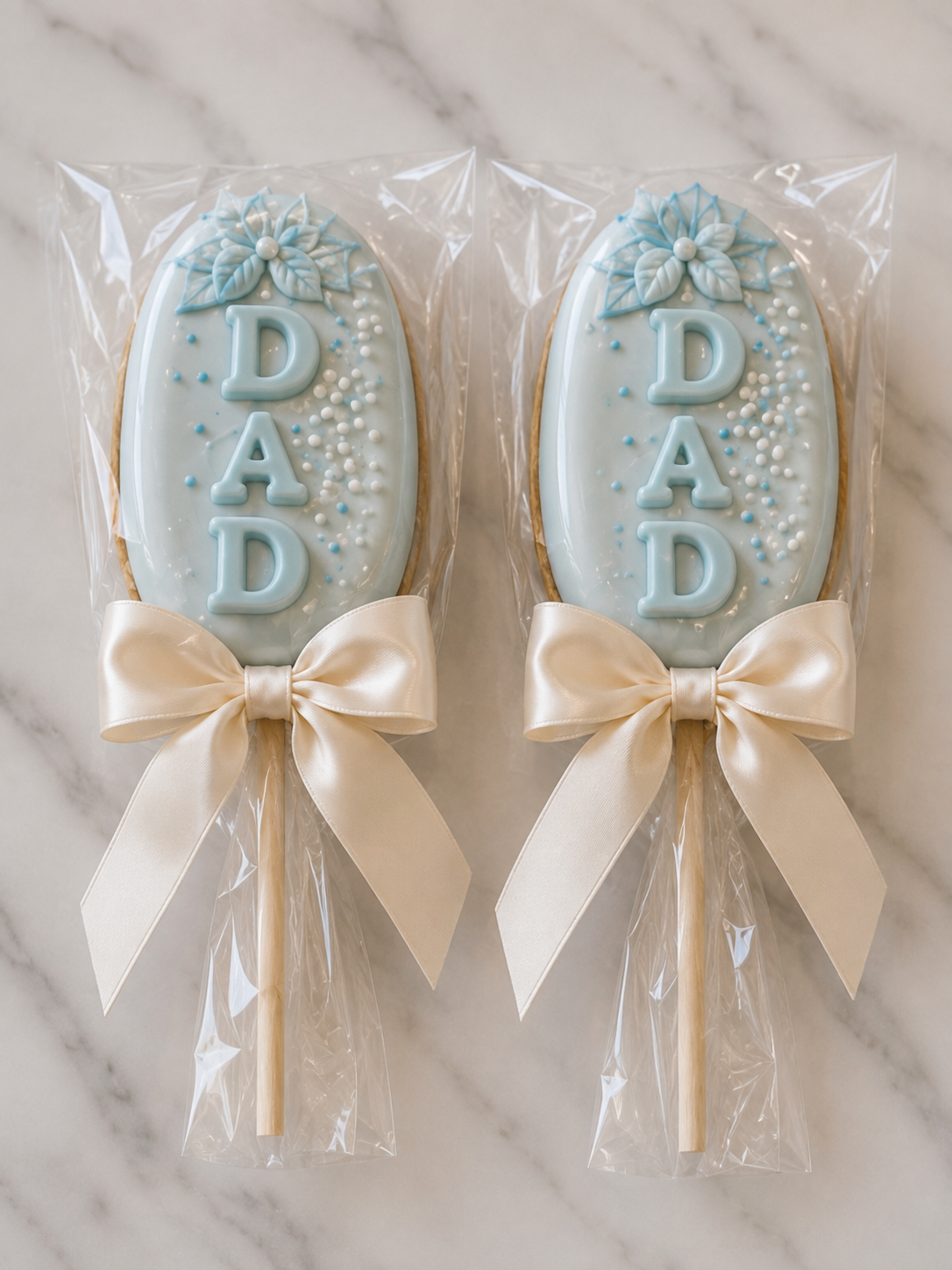 Custom blue and white cakesicles decorated with floral details, pearl sprinkles and DAD lettering for a Father's Day ecial event.