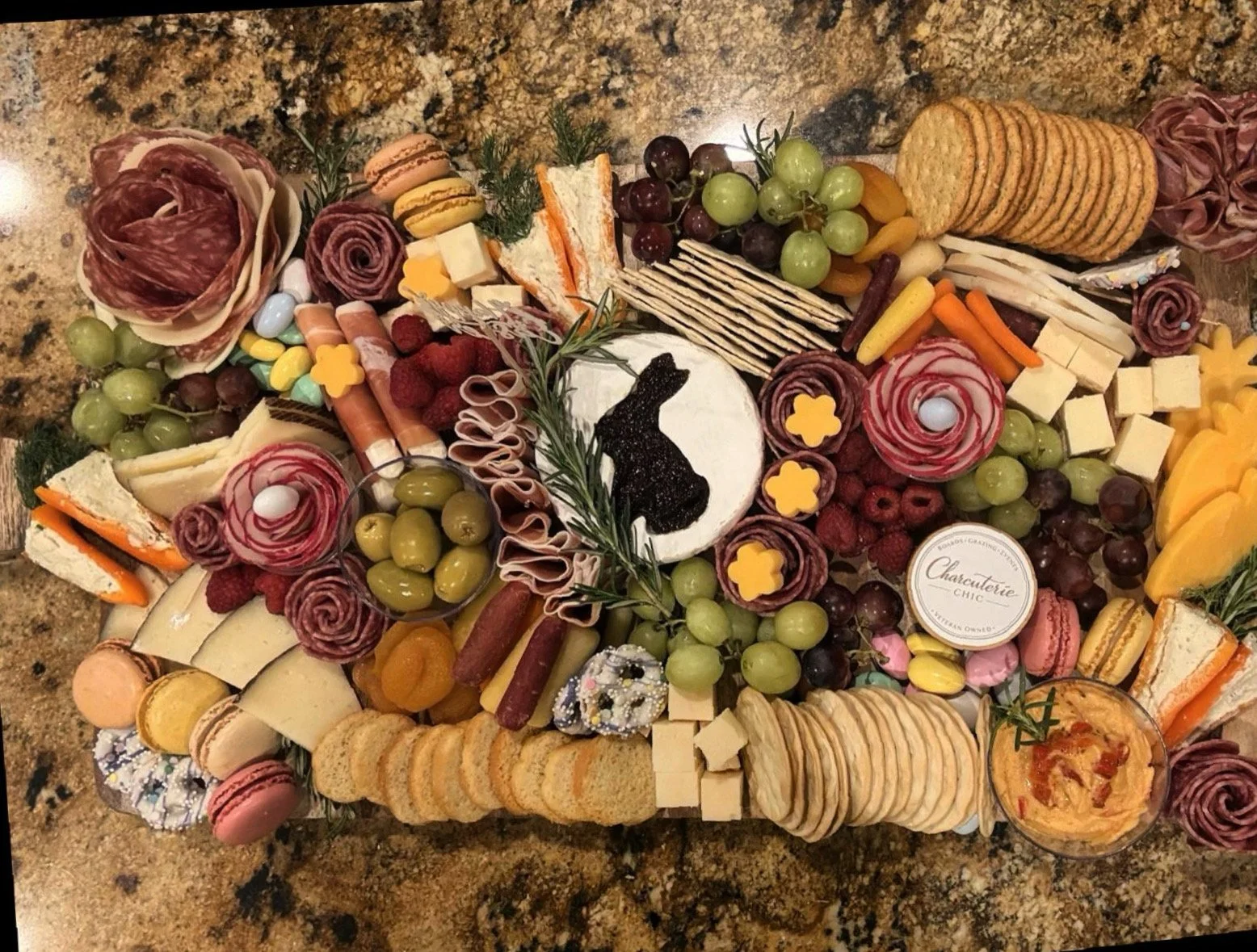 Easter charcuterie board with artisan cheeses, cured meats, fresh fruit, crackers, macarons and festive spring details including a bunny design.