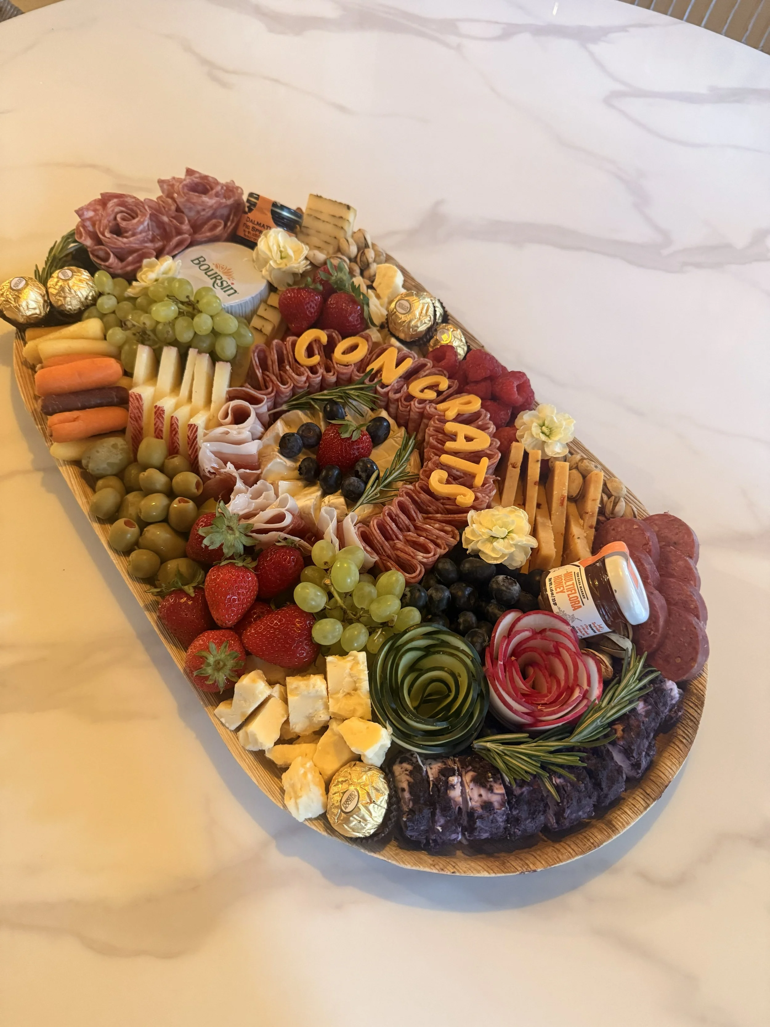 Congratulations charcuterie board with artisan cheeses, cured meats, fresh fruit, olives and personalized lettering for a special celebration in San Antonio.