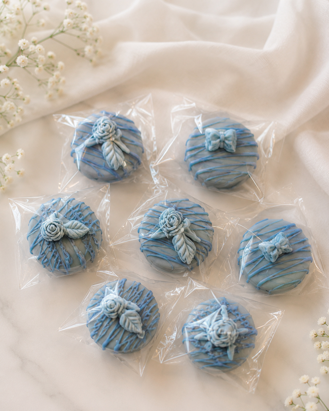 Chocolate-covered Oreos decorated in soft blue tones with delicate drizzle, floral details, bows, and elegant handcrafted accents.