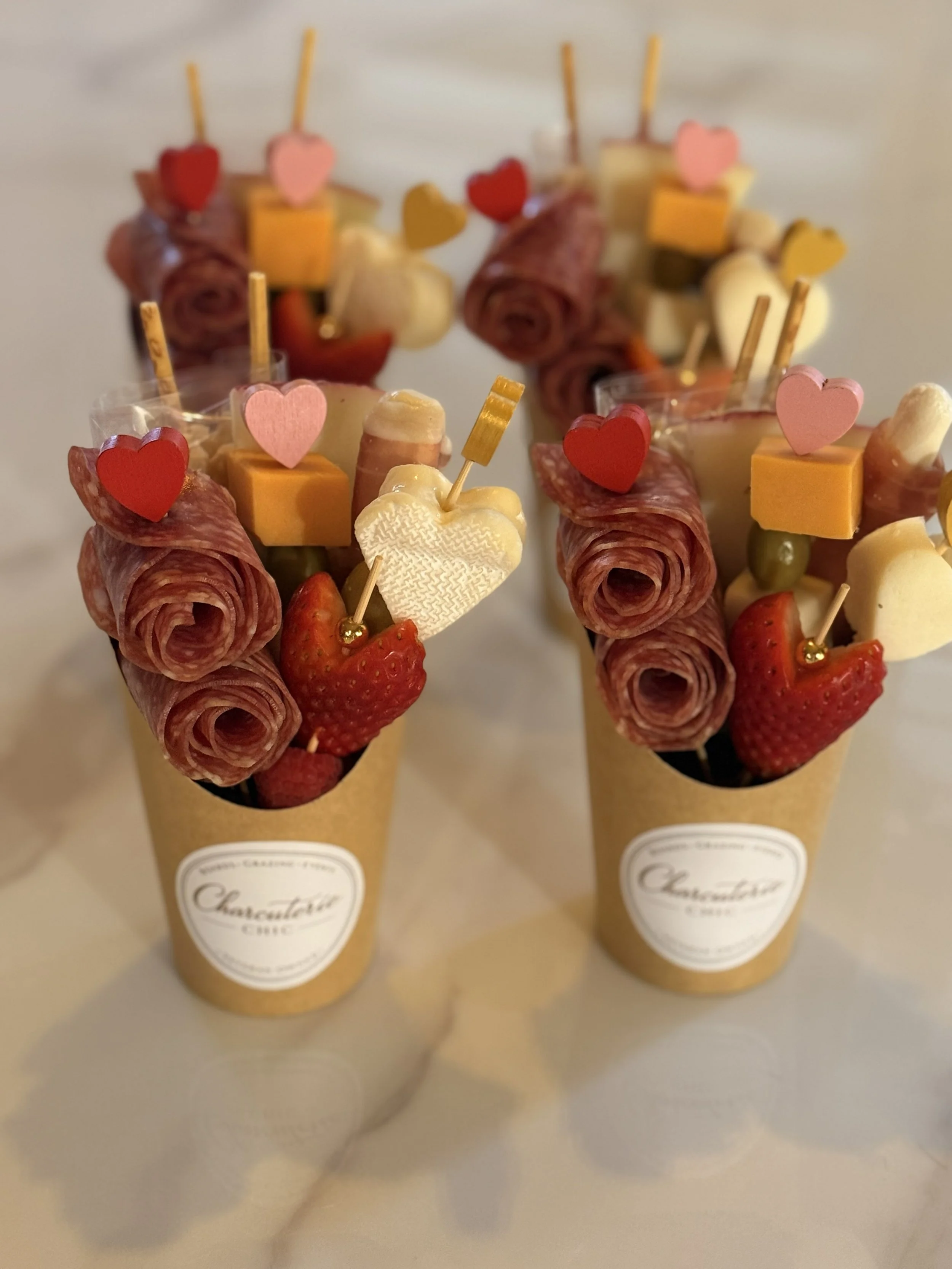 Valentine’s Day charcuterie cups with salami roses, artisan cheeses, strawberries, olives and heart-shaped details by Charcuterie Chic.