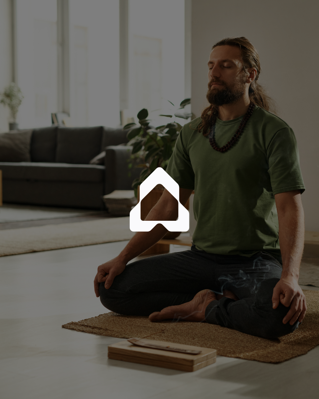 Person meditating in a living room, seated in a cross-legged position on a rug with a wooden box and incense in front.