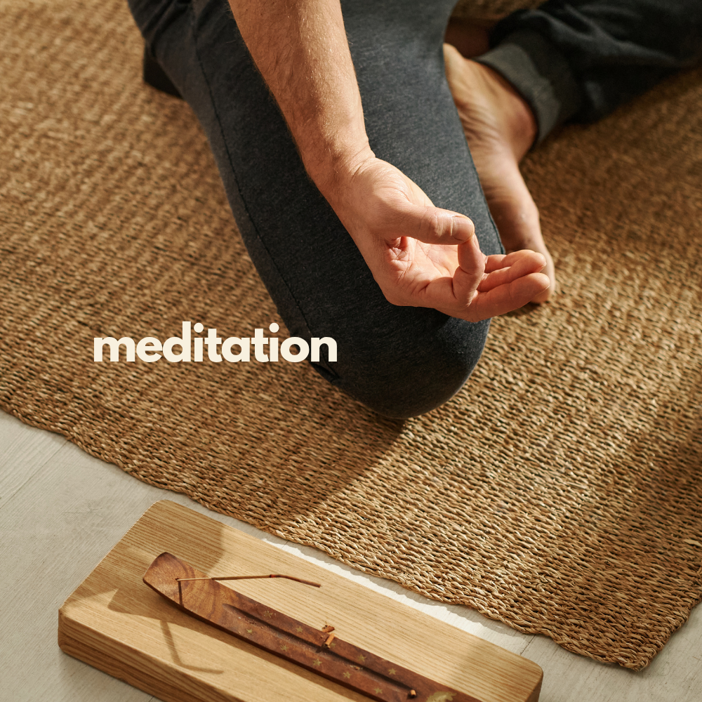 A person practicing meditation on a textured brown mat, seated with legs crossed and hand resting on the knee in a mudra gesture. A wooden incense holder with a lit incense stick is placed nearby.
