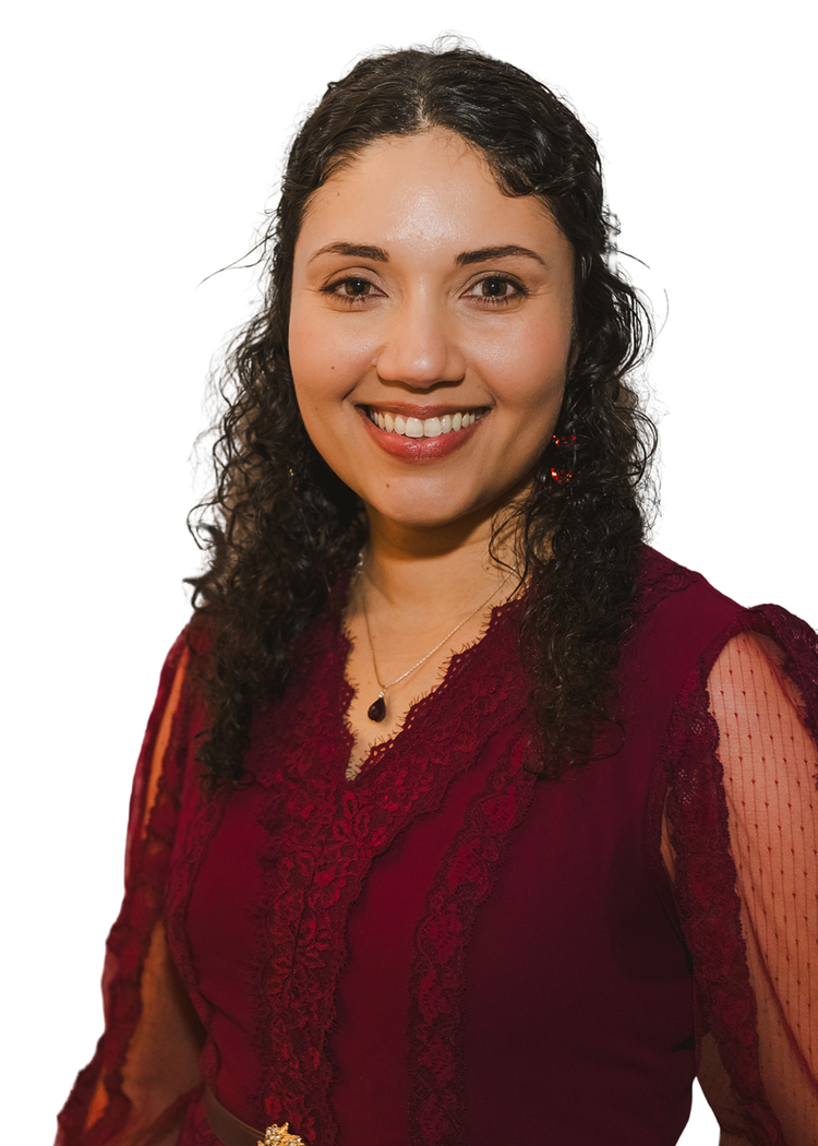 A woman with curly dark hair smiling, wearing a velvet and lace burgundy dress with a small pendant necklace, against a white background.