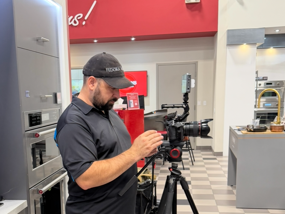 Man adjusting camera equipment in a modern kitchen showroom.