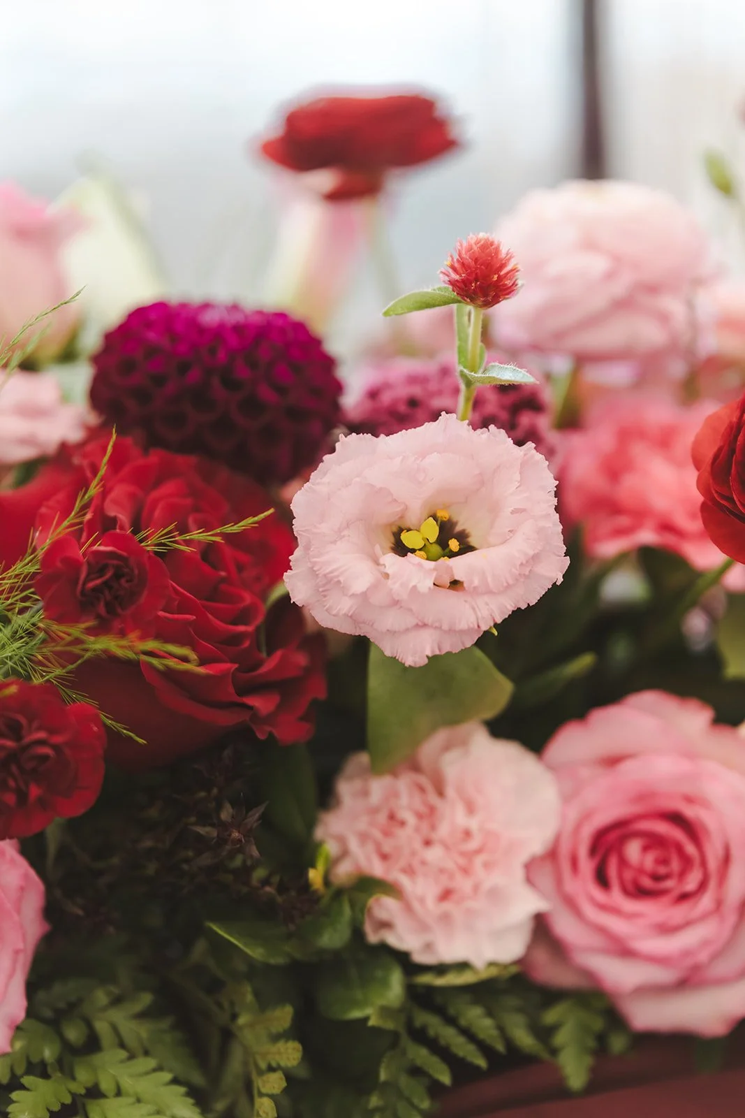 A close-up of a mixed bouquet of pink, red, and purple flowers, including roses and lisianthus, with greenery.