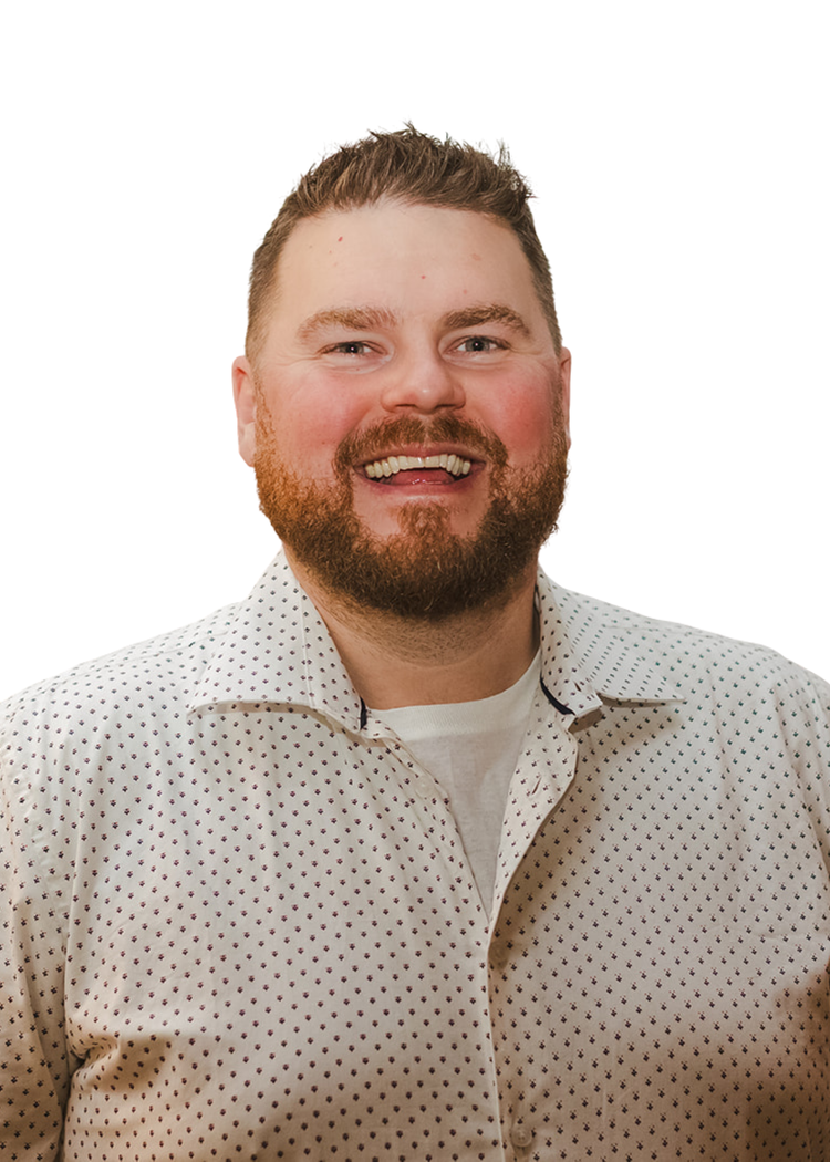 A smiling man with a beard and short light brown hair wearing a white polka-dotted shirt.