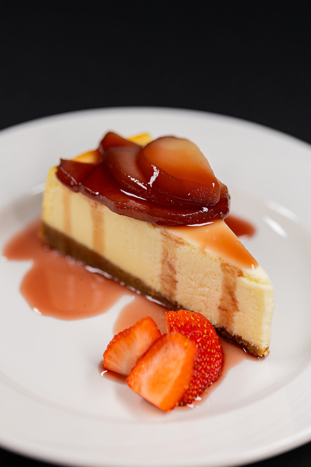 A slice of cheesecake with strawberry topping and sliced strawberries on a white plate.
