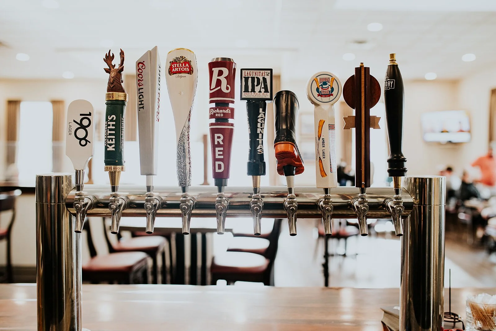 A row of beer tap handles on a bar counter, each with different labels and designs, in a bar or pub setting.