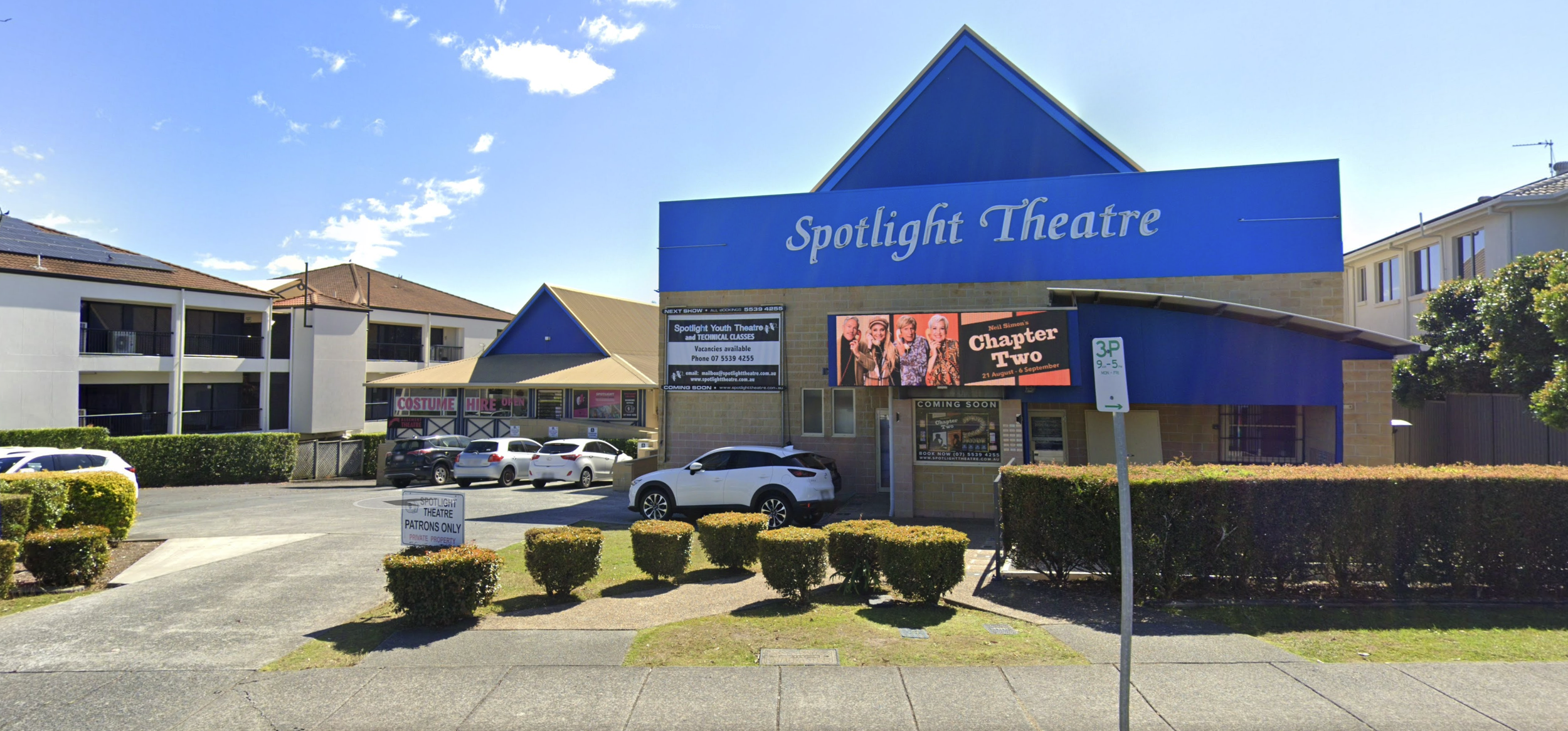 Exterior view of Spotlight Theatre with parking lot, show advertisements, and nearby residential buildings.