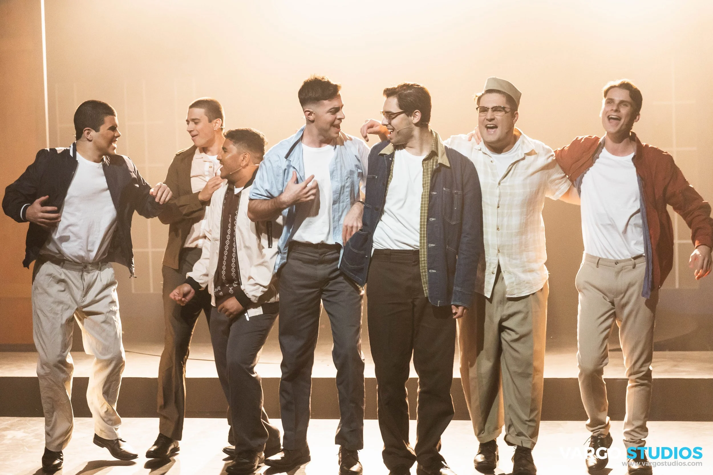 A group of seven young men enjoying a moment together on stage with warm lighting.