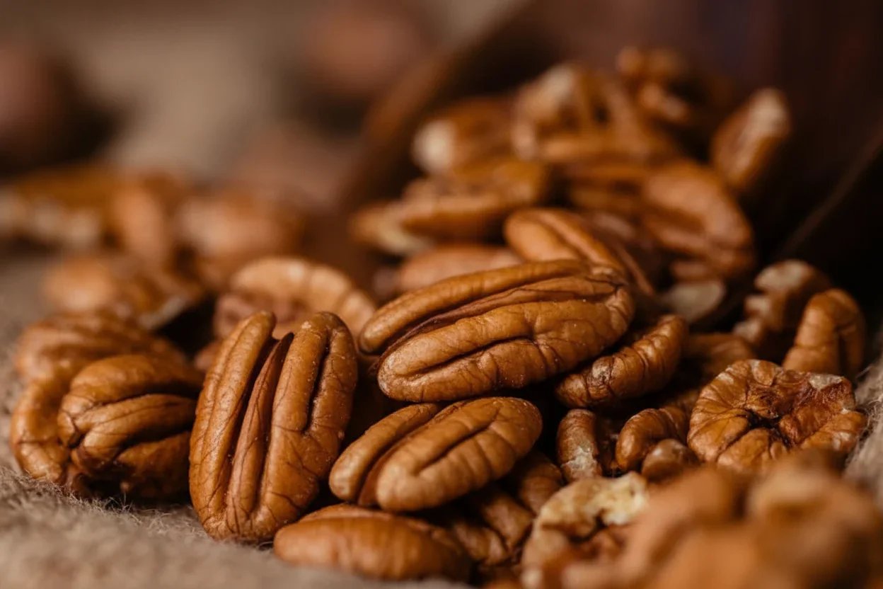Close-up of scattered roasted pecans on a textured surface.