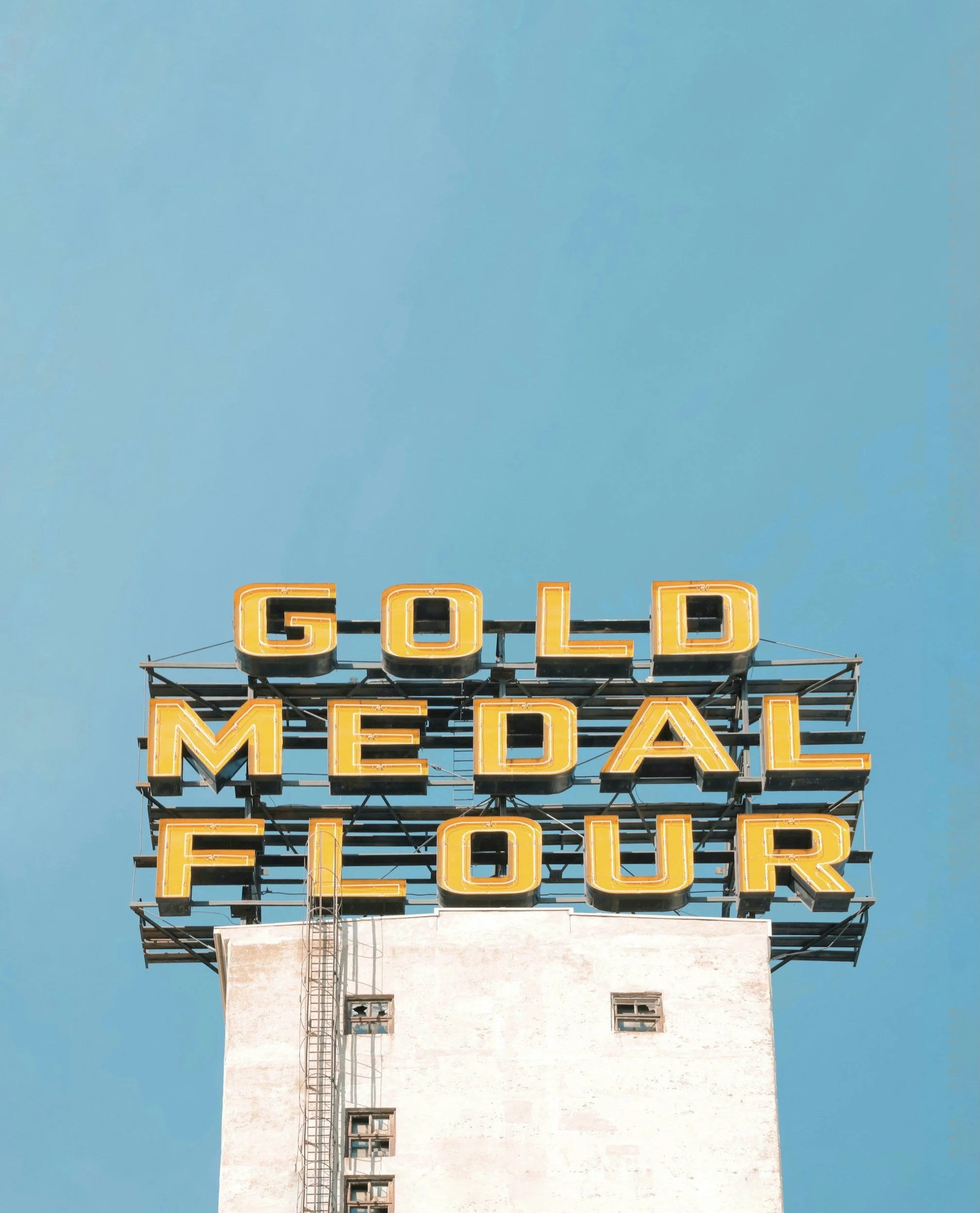 Neon sign reading 'GOLD MEDAL FLOUR' against a blue sky.