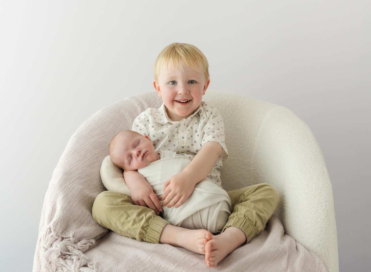 Sibling holding newborn baby during newborn photography session in Bishopdale studio