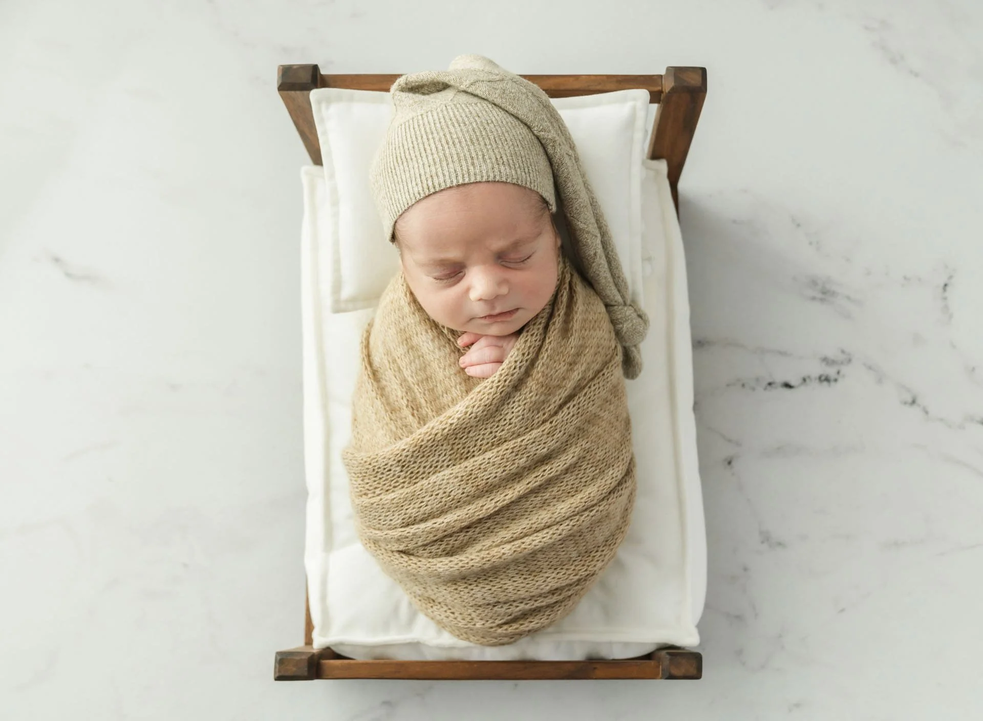 Sleeping newborn baby in soft neutral tones photographed in tiny bed prop at Christchurch studio
