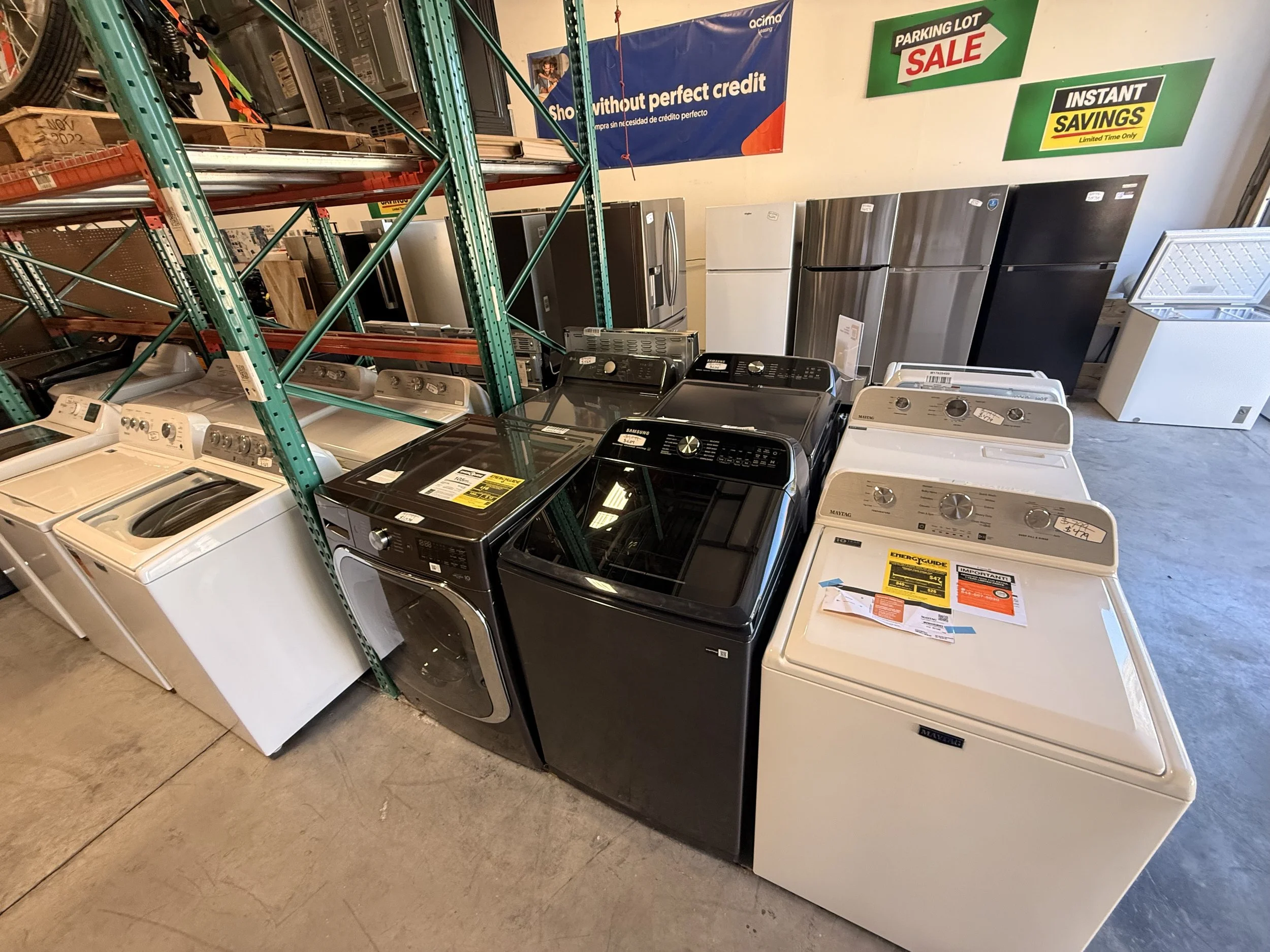 A display of washing machines and refrigerators in a store aisle with various sale and savings signs on the wall.