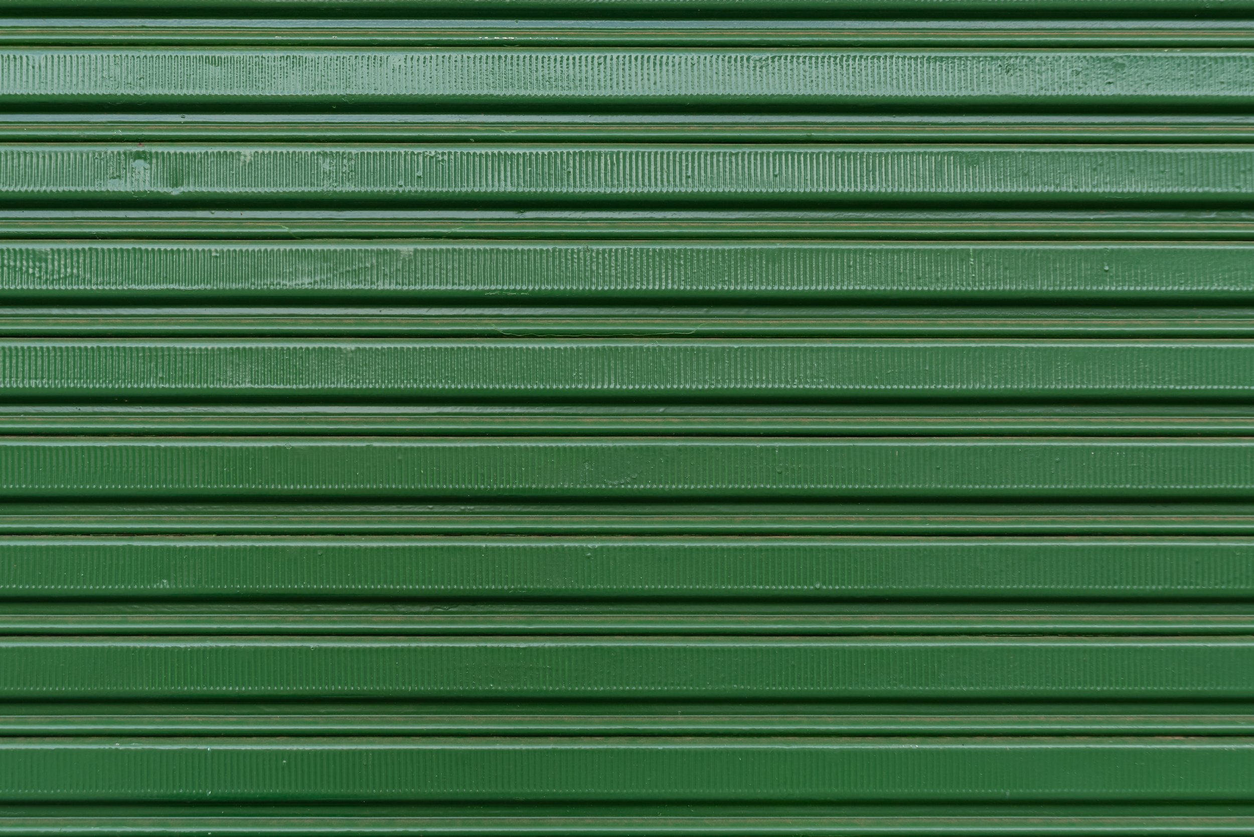 Green metal rolling shutter with horizontal lines and textured surfaces.