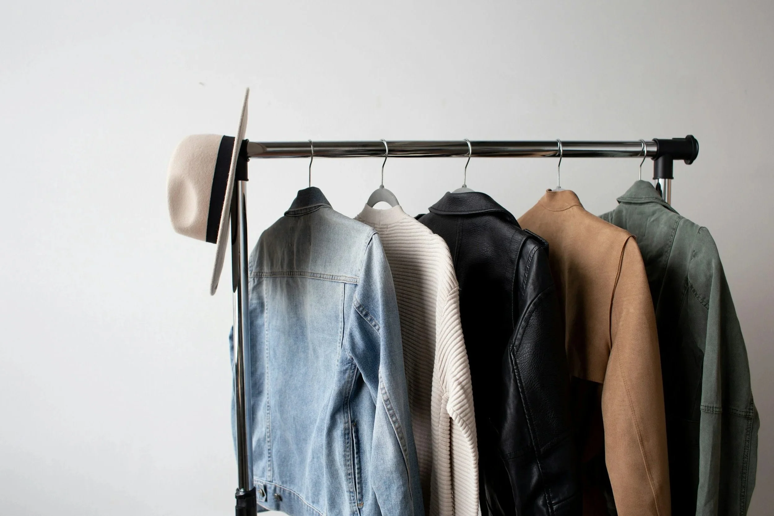 Clothing rack holding five jackets and a hat, white wall background