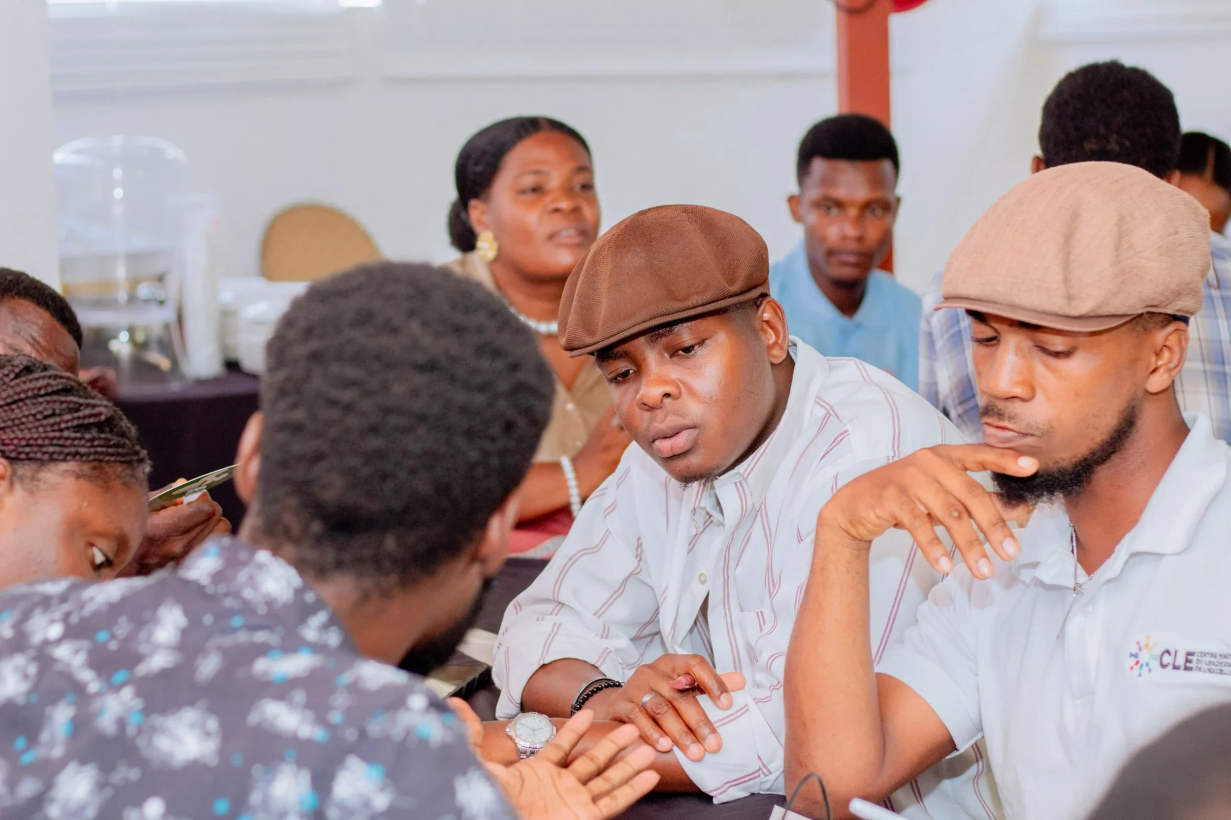 Group of people engaged in a discussion or activity at a table during an event, with some looking serious or focused.