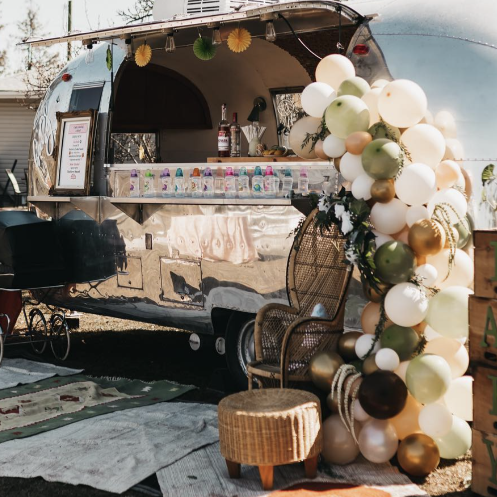A photo of an airstream with balloons, greenery, rugs and decor, setup for an event.