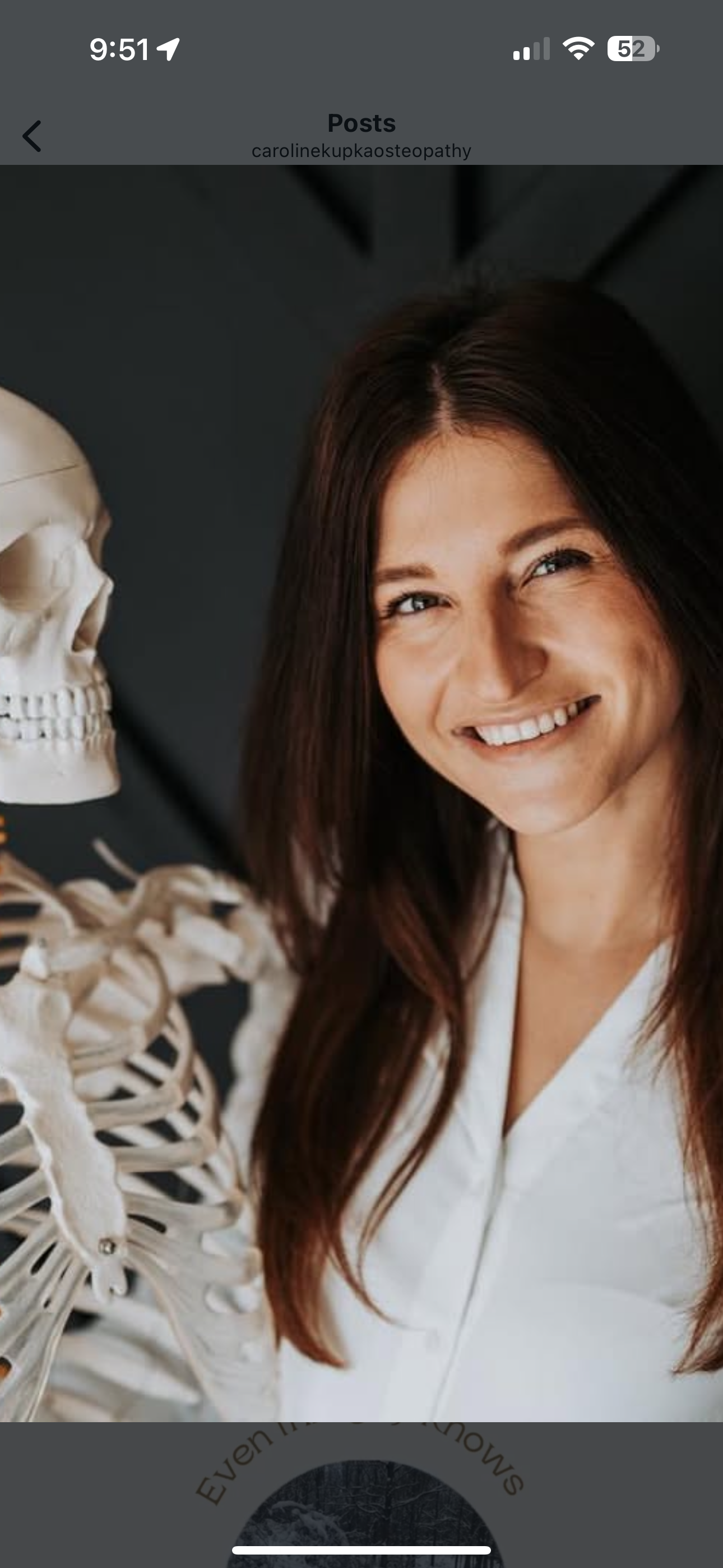 A photo of Caroline, an osteopath, standing beside a model of a human skeleton.