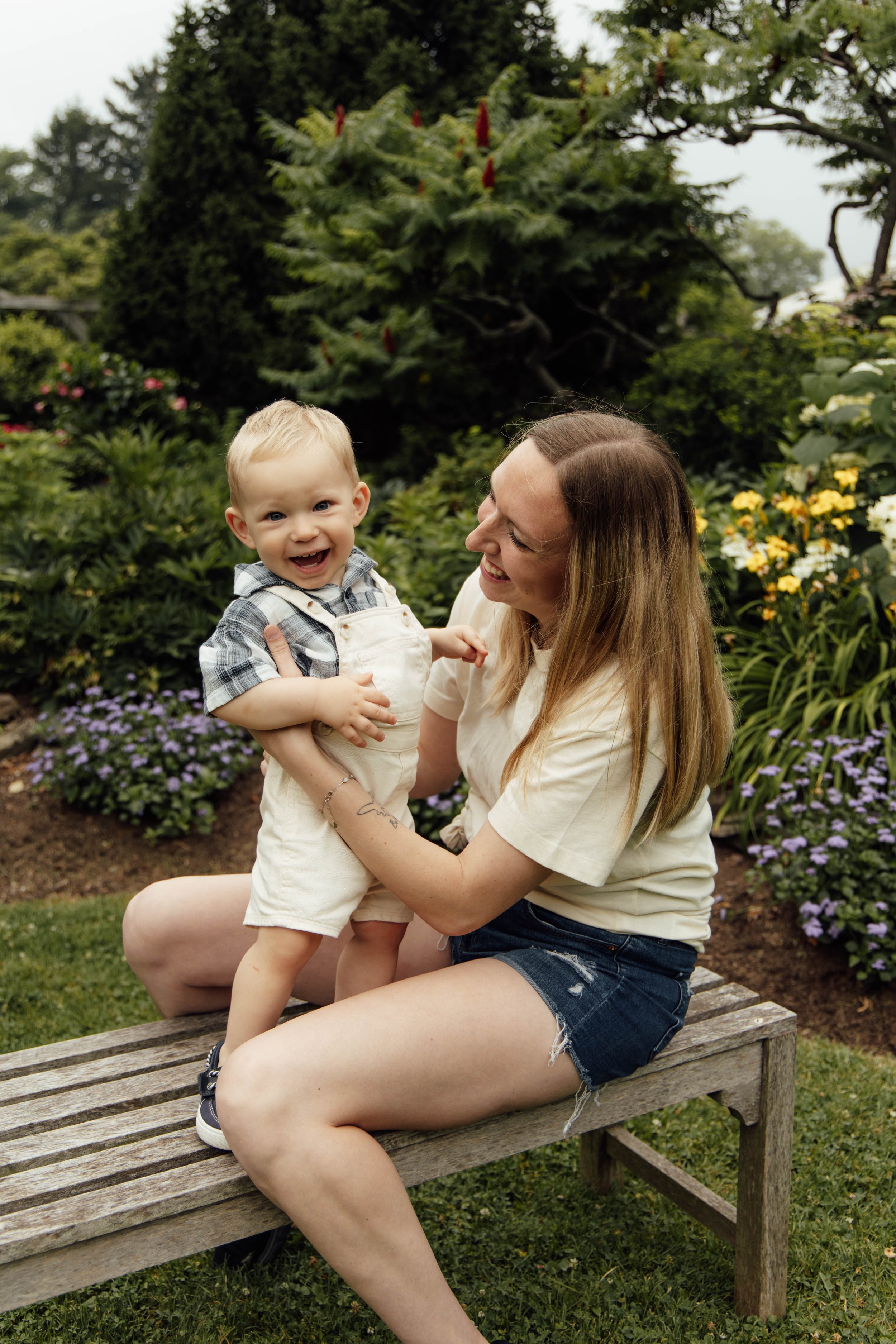 A woman holding a young boy in a garden with colorful flowers and green bushes, smiling and enjoying the moment.