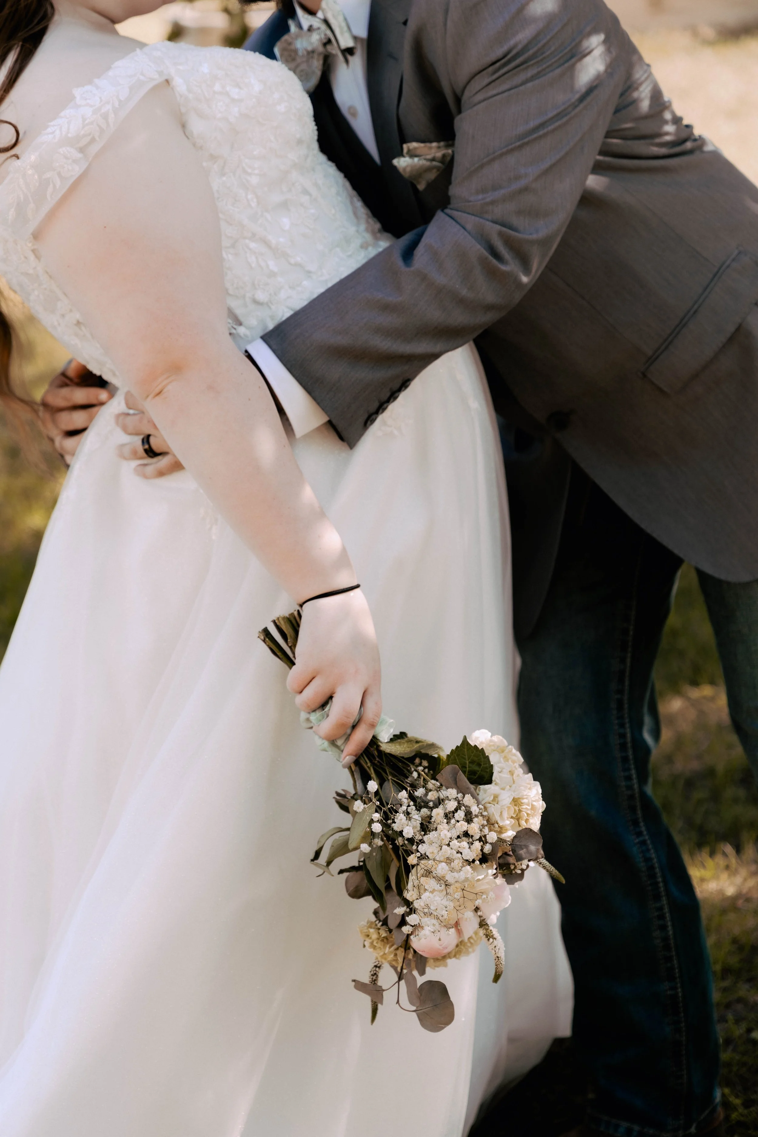 A bride in a wedding dress holding a bouquet of flowers while a groom in a gray suit leans in close during a wedding ceremony.