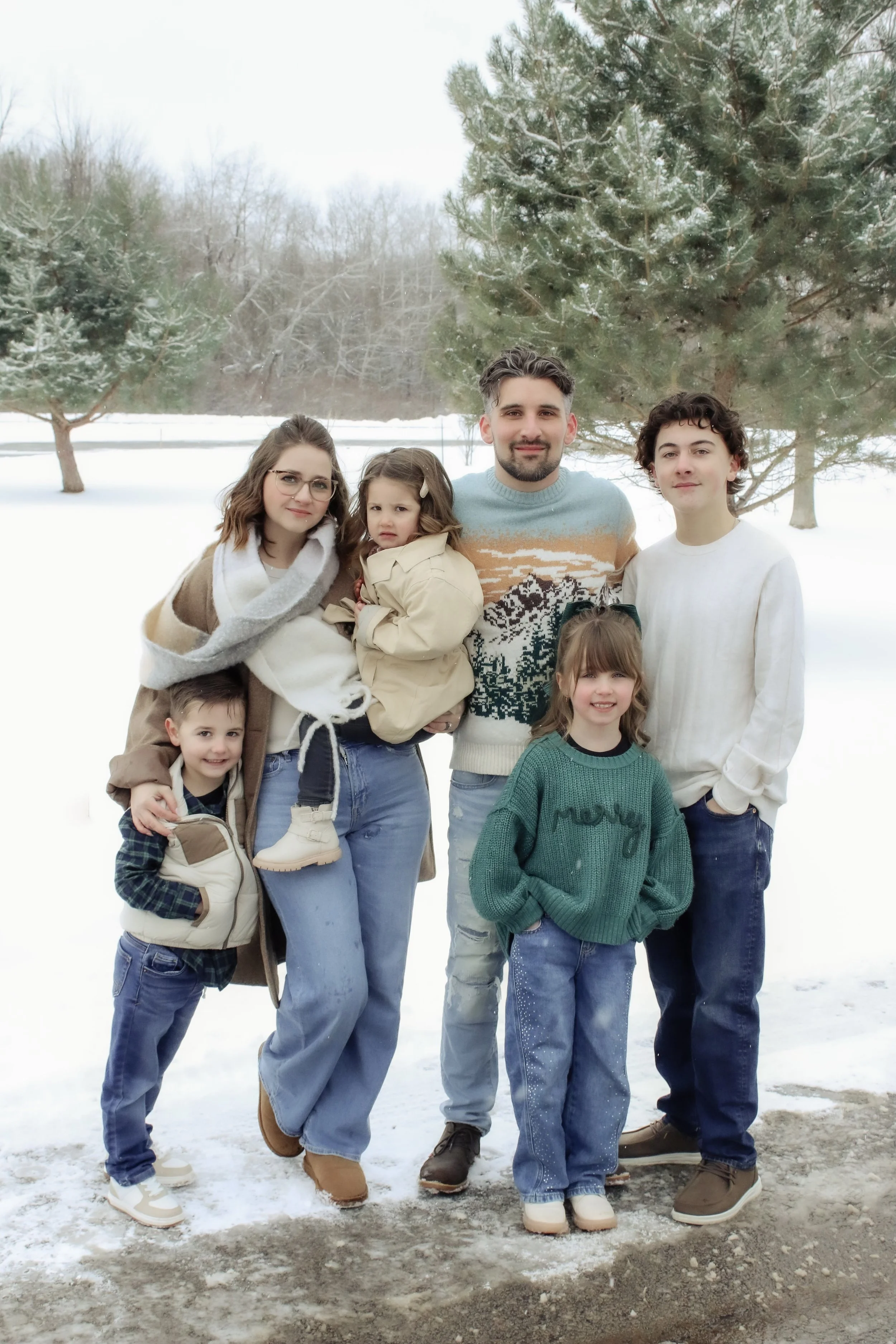 Family of seven outside in snow, with evergreen trees in the background