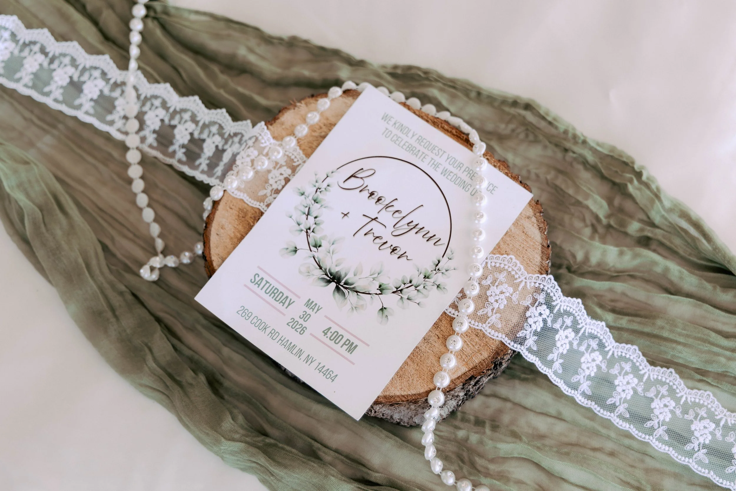 Wedding invitation with lace and pearl decorations, placed on a wooden surface, with event details visible.