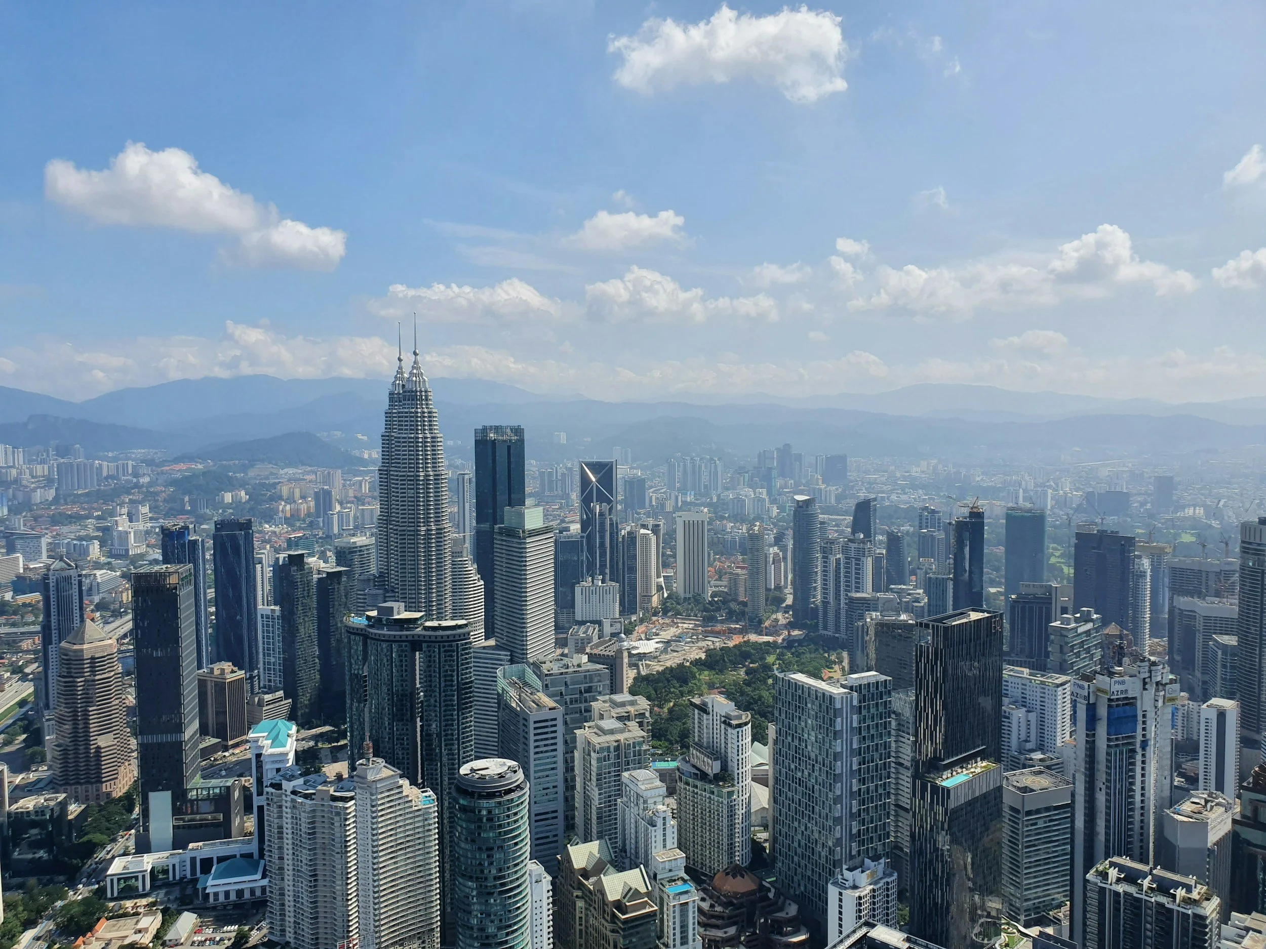 Skyline view of Kuala Lumpur with the Petronas Towers and surrounding skyscrapers, under a partly cloudy sky.