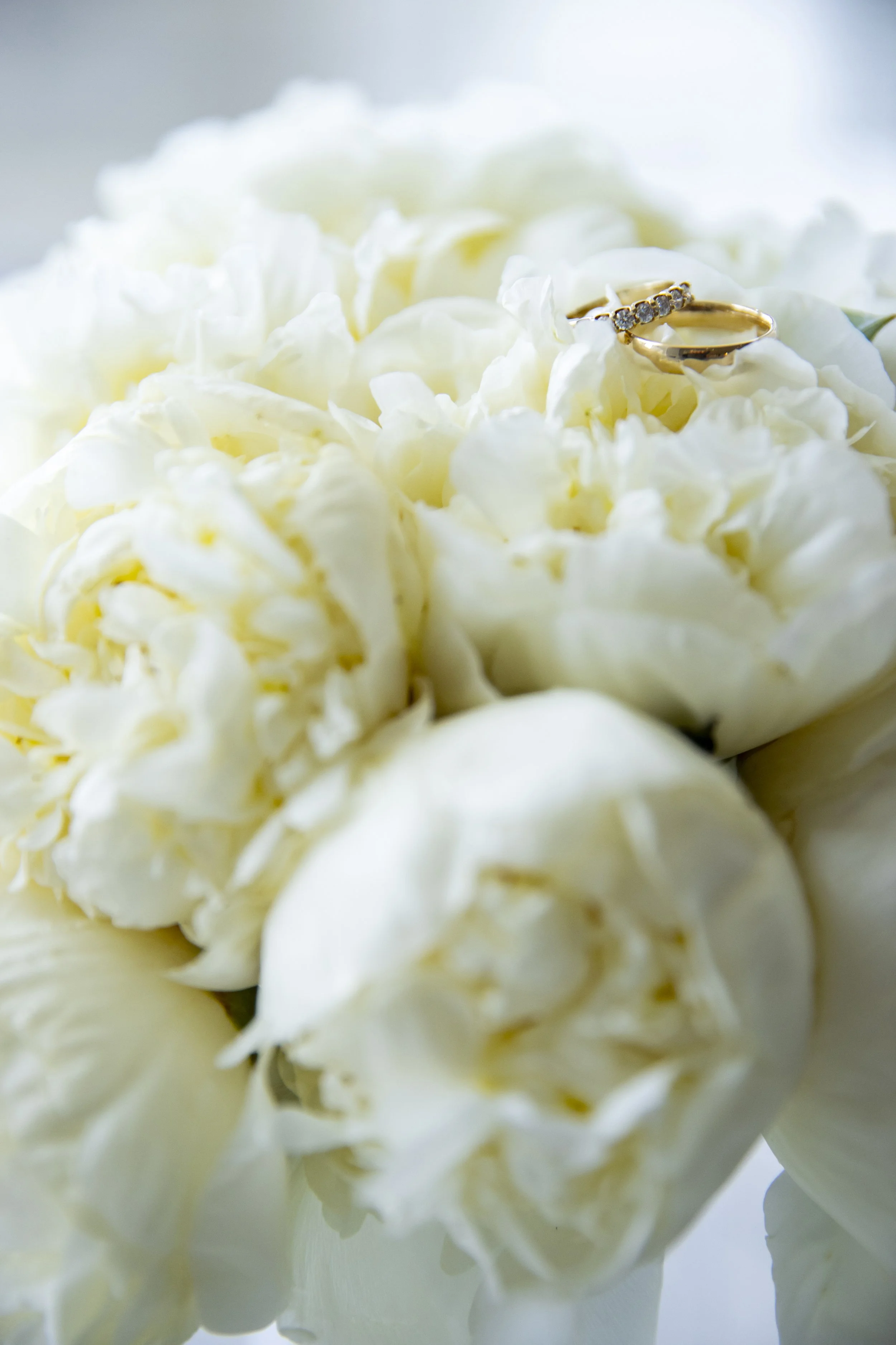 A bouquet of white flowers with a gold ring resting on top.