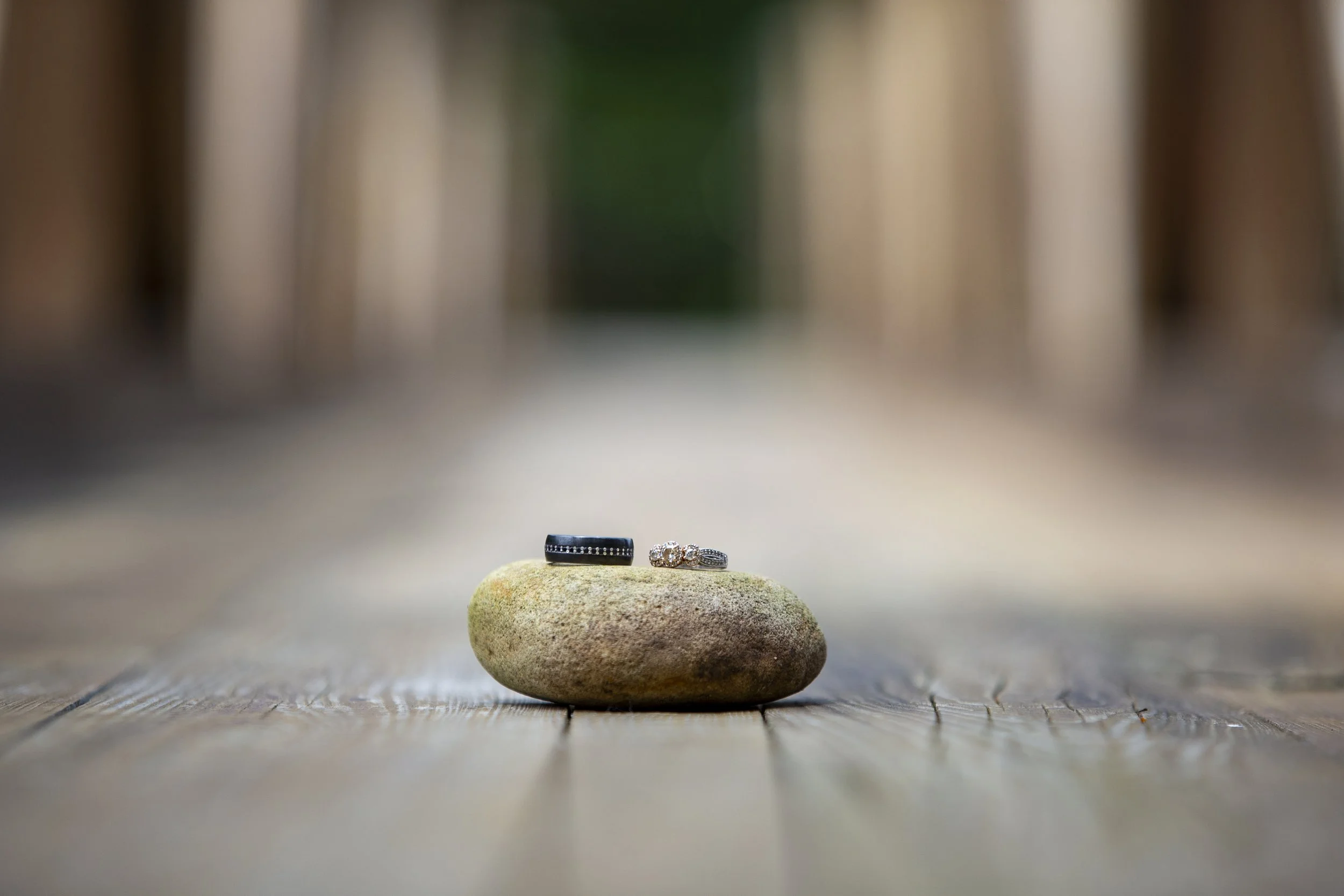 Three rings placed on a smooth stone on a wooden surface, with a blurred background.