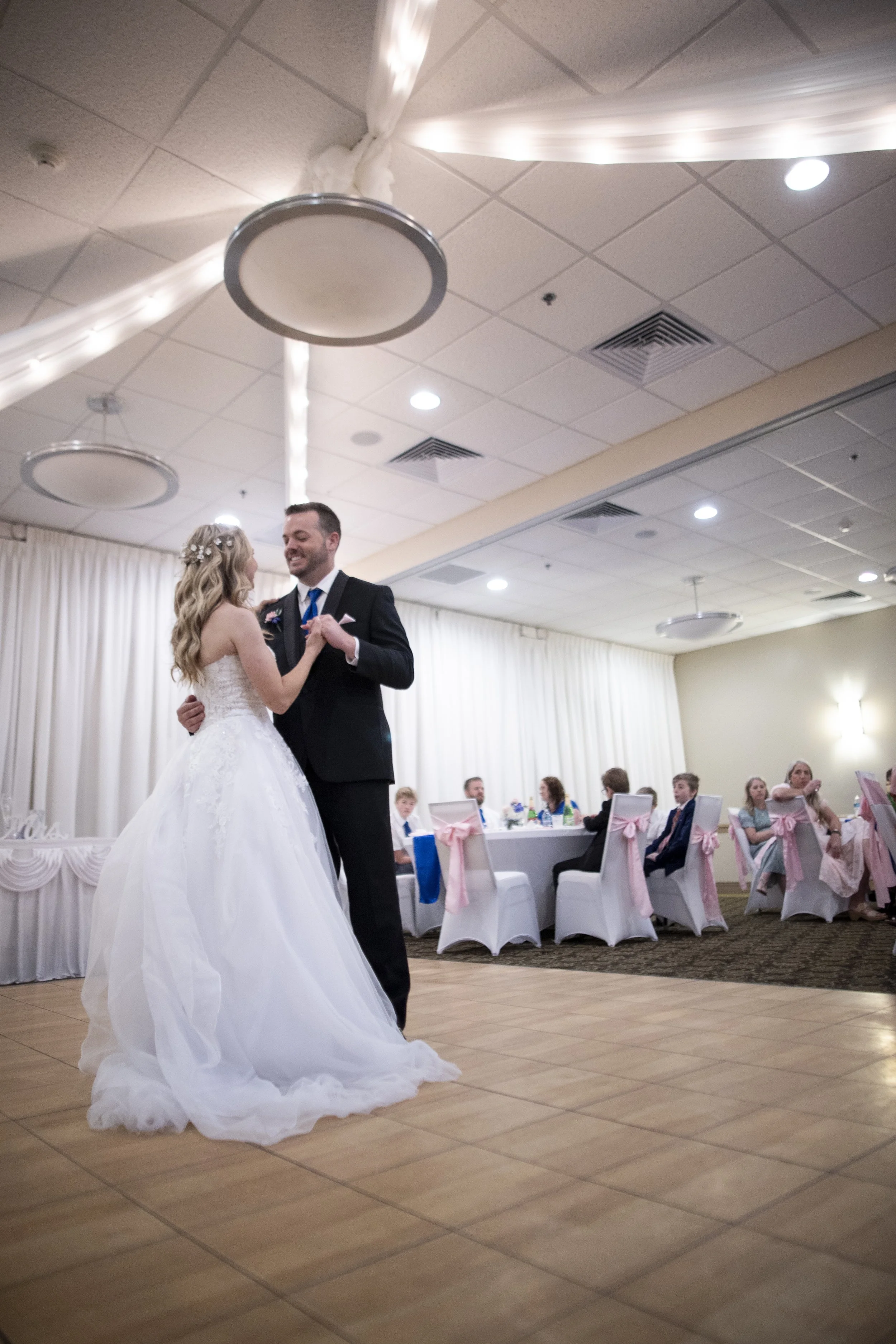 A bride and groom sharing a dance at their wedding reception, with guests seated at decorated tables in the background.