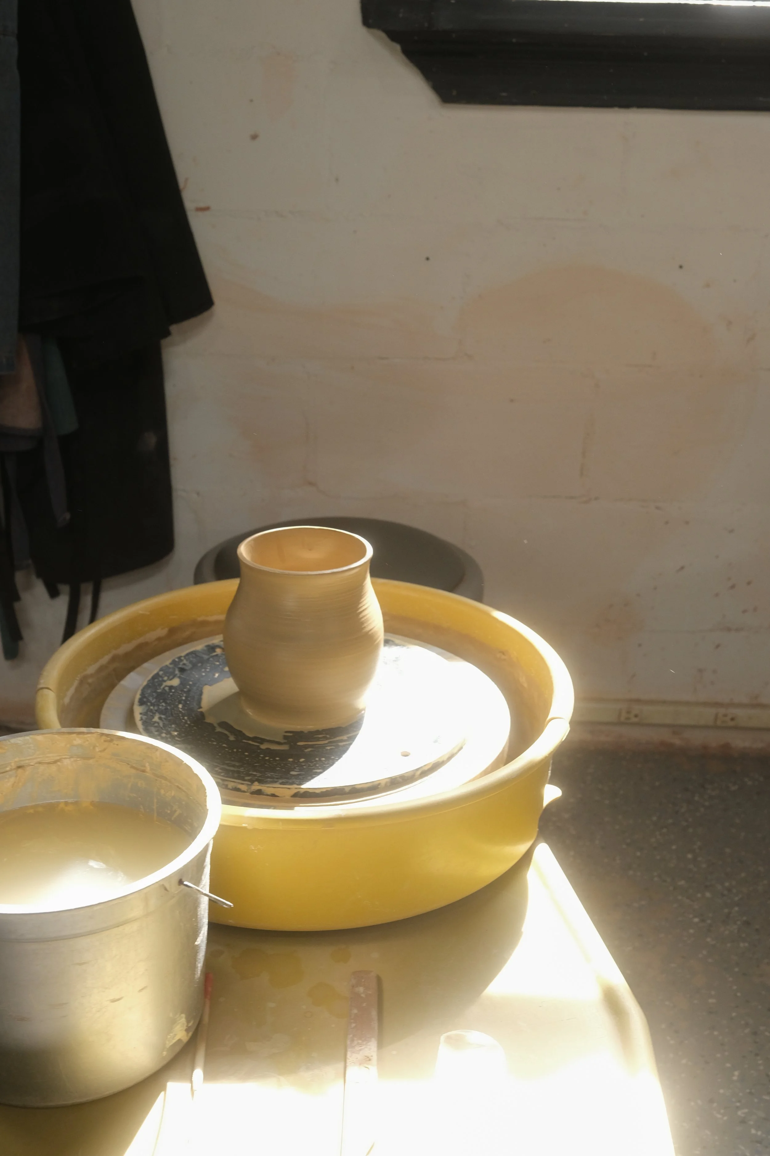 A ceramic vase on a pottery wheel in a ceramics studio, with sunlight hitting the workspace.