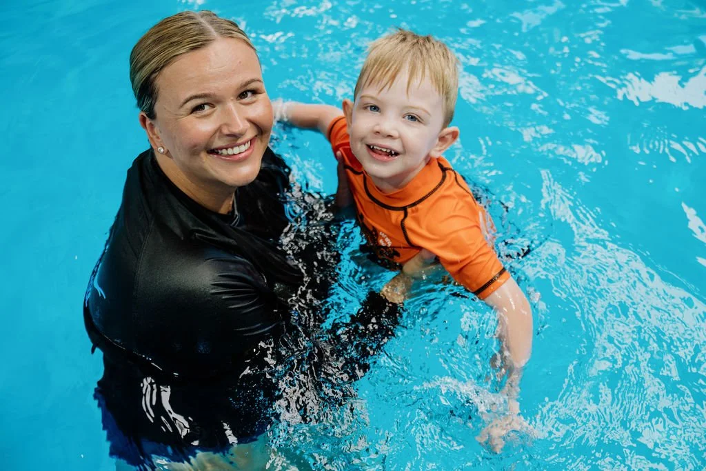 A woman and a young boy smiling and playing in a swimming pool.
