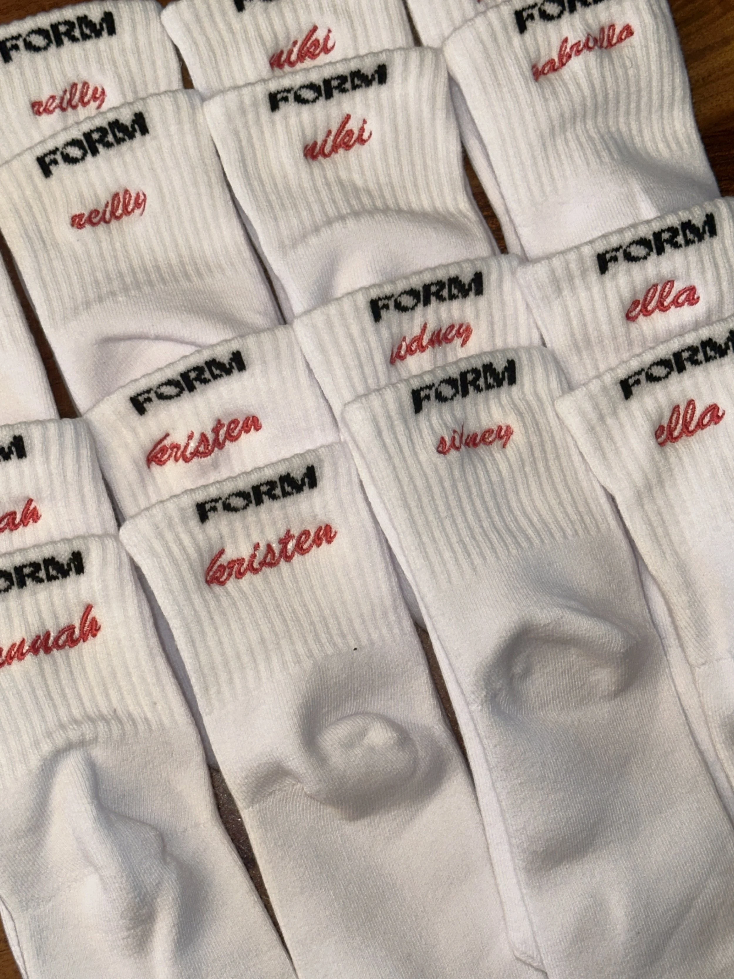 White crew socks with embroidered text reading 'FORM' in black and a name in red, repeated in a pattern.