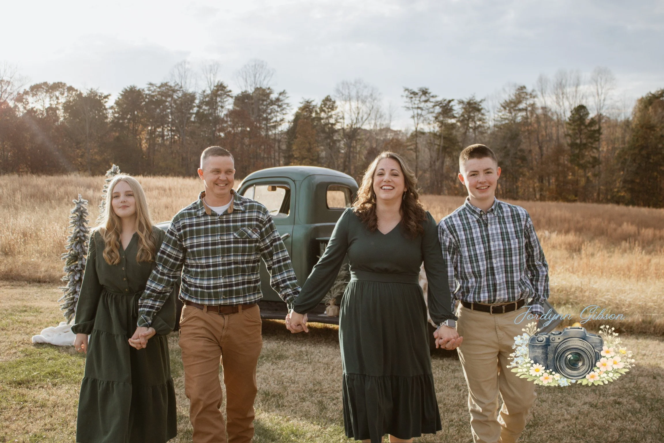 A family of five holding hands and walking outdoors in a field with trees in the background, smiling and enjoying the moment.