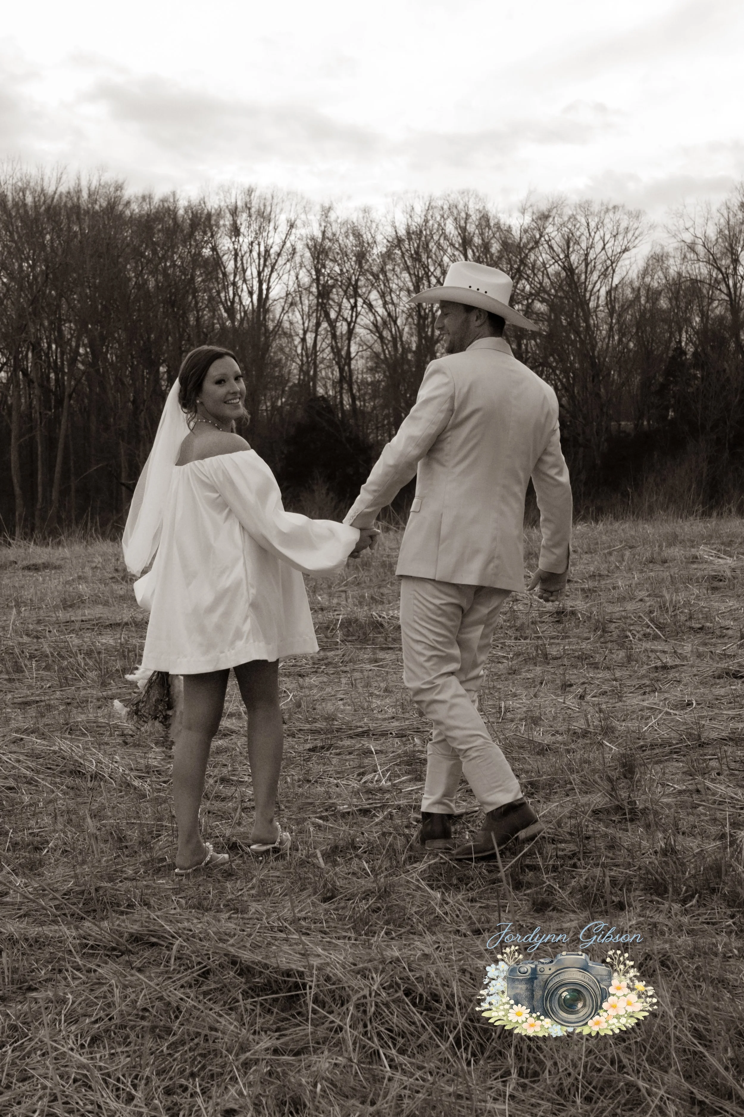 Couple standing in a field with a veil in a white dress. Elopement Photography Sophia NC Couple walking in a field Holding hands