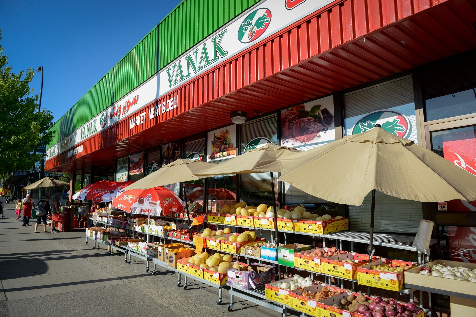 Outdoor market stand with produce, umbrellas, and customers in front of a grocery store named Vanak in Central Lonsdale North Vancouver.