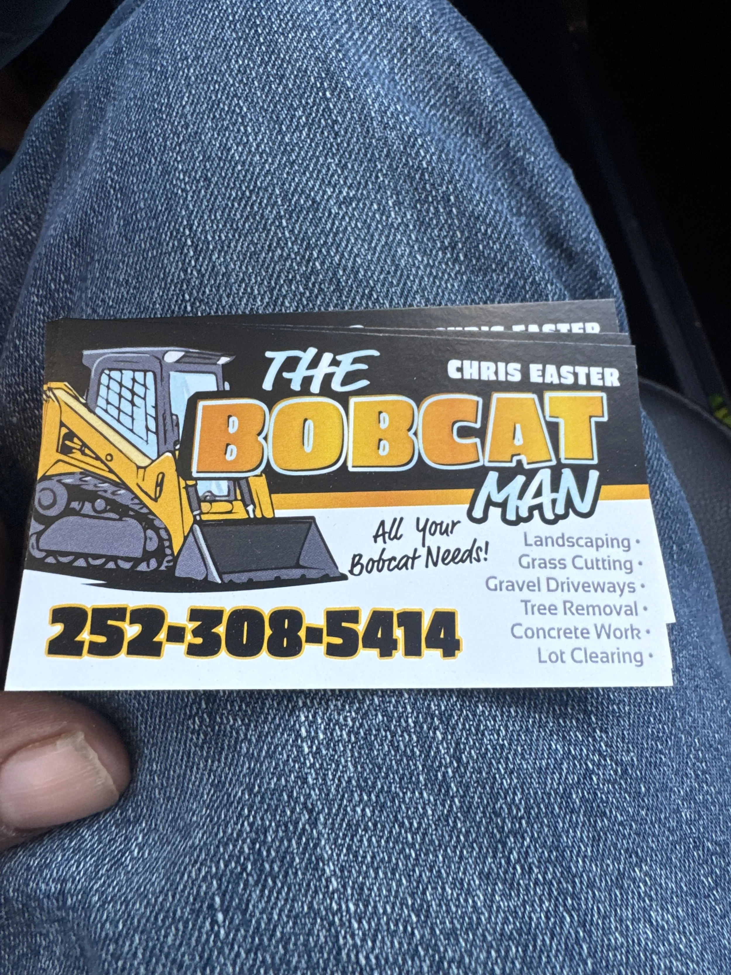 Business card for The Bobcat Man featuring a cartoon illustration of a yellow Bobcat skid-steer loader and providing services such as landscaping, grass cutting, gravel driveways, tree removal, concrete work, and lot clearing. Phone number is 252-308-5414.