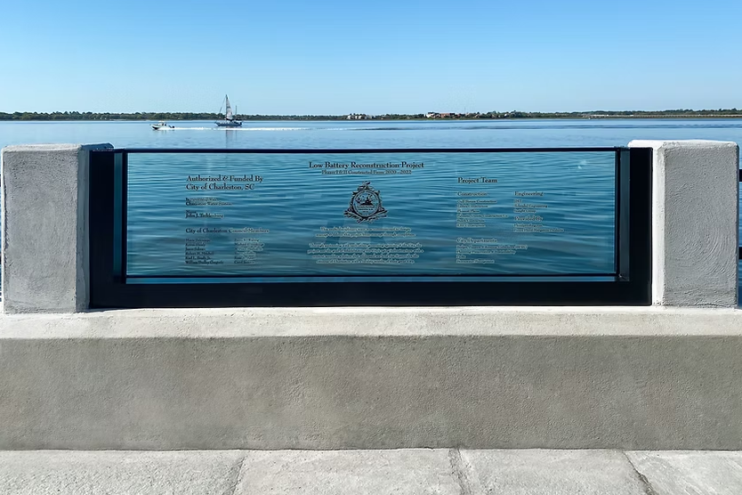 Permanent flood-resistant glass barrier installed along waterfront pedestrian walkway for unobstructed flood protection.