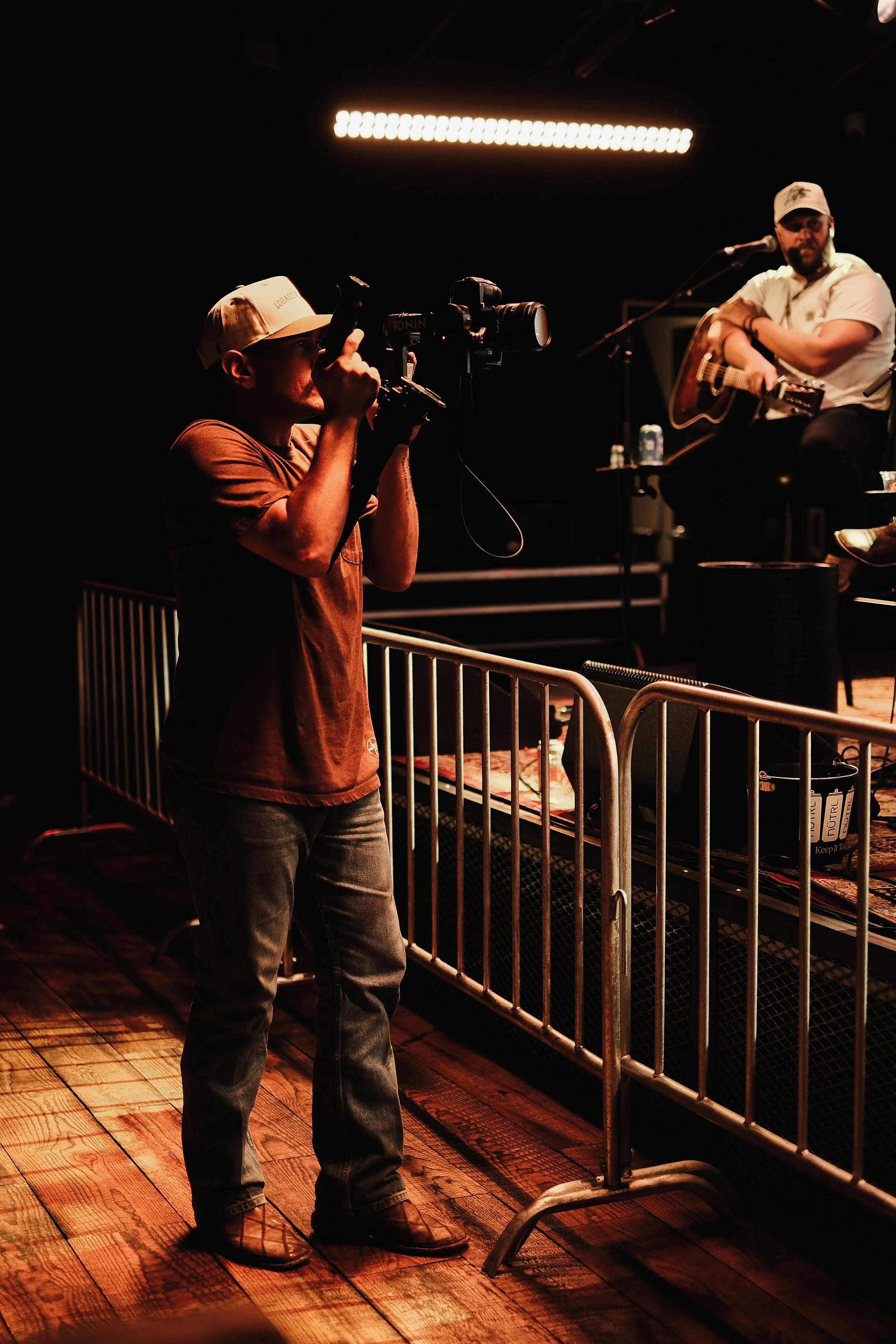 A cameraman filming a musician playing guitar on stage during a live performance.