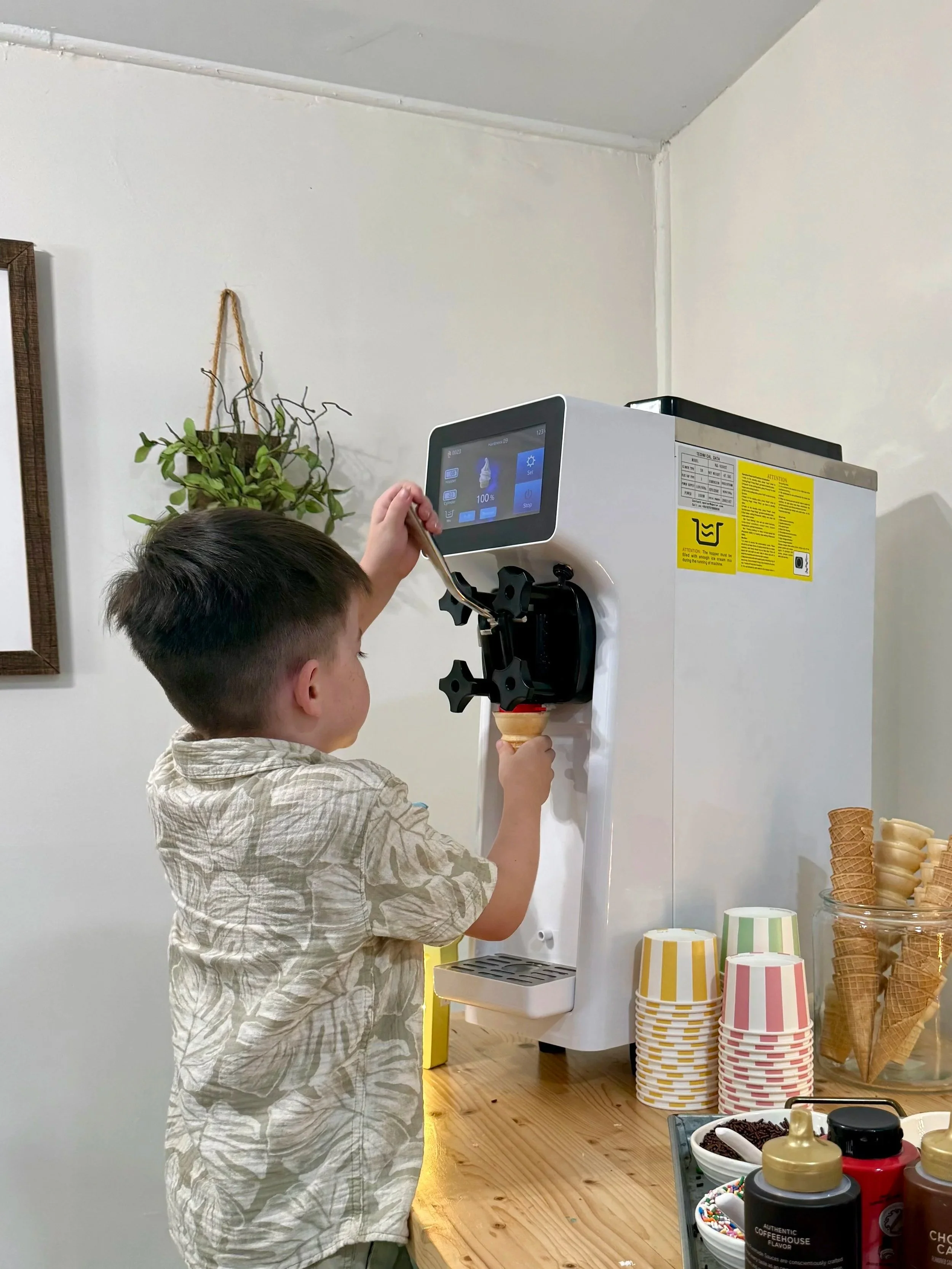 Boy uses soft serve machine to make ice cream cone.