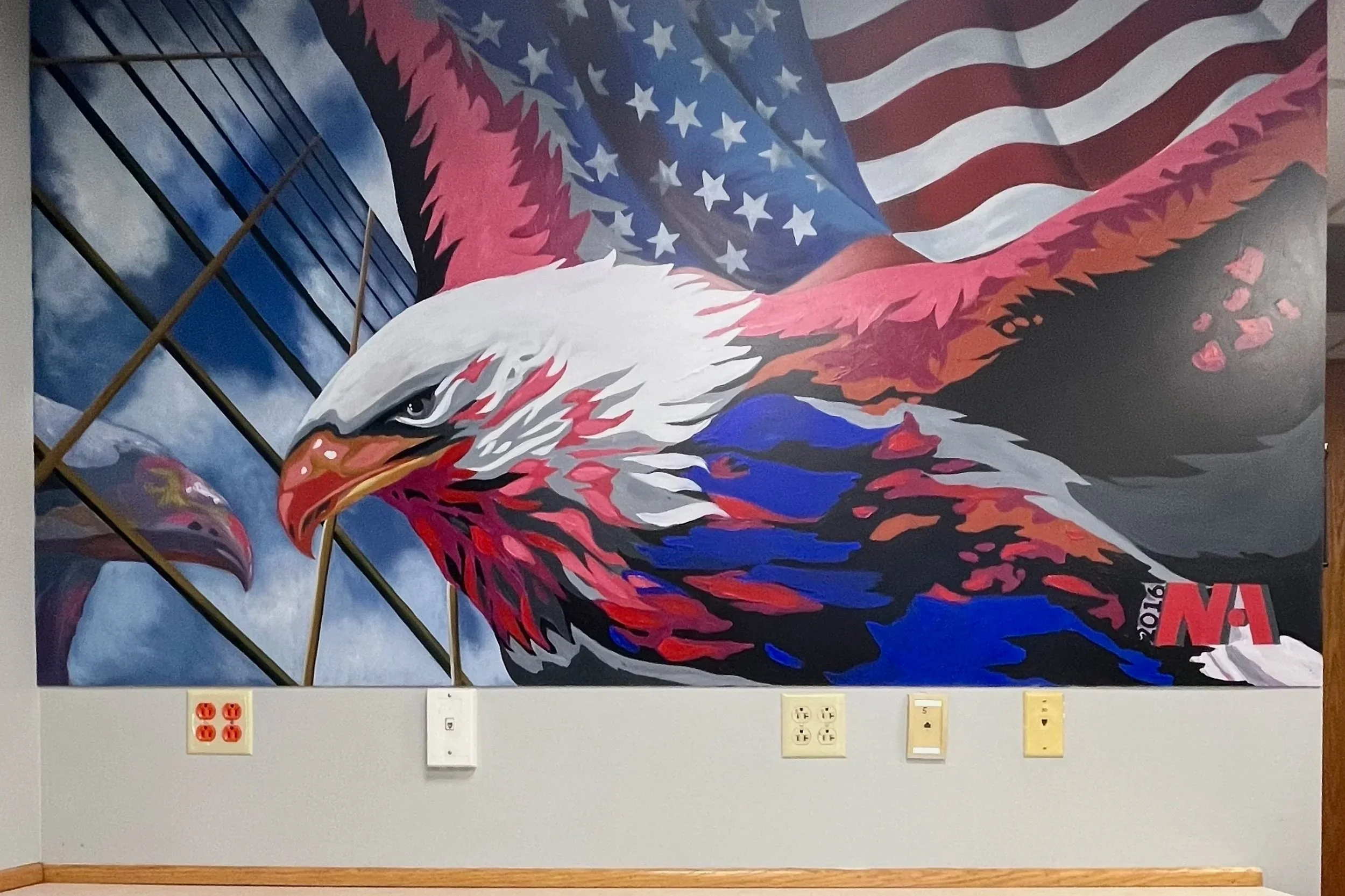 Painting of an eagle with American flag patterns in the background, mounted on a wall with electrical outlets below.