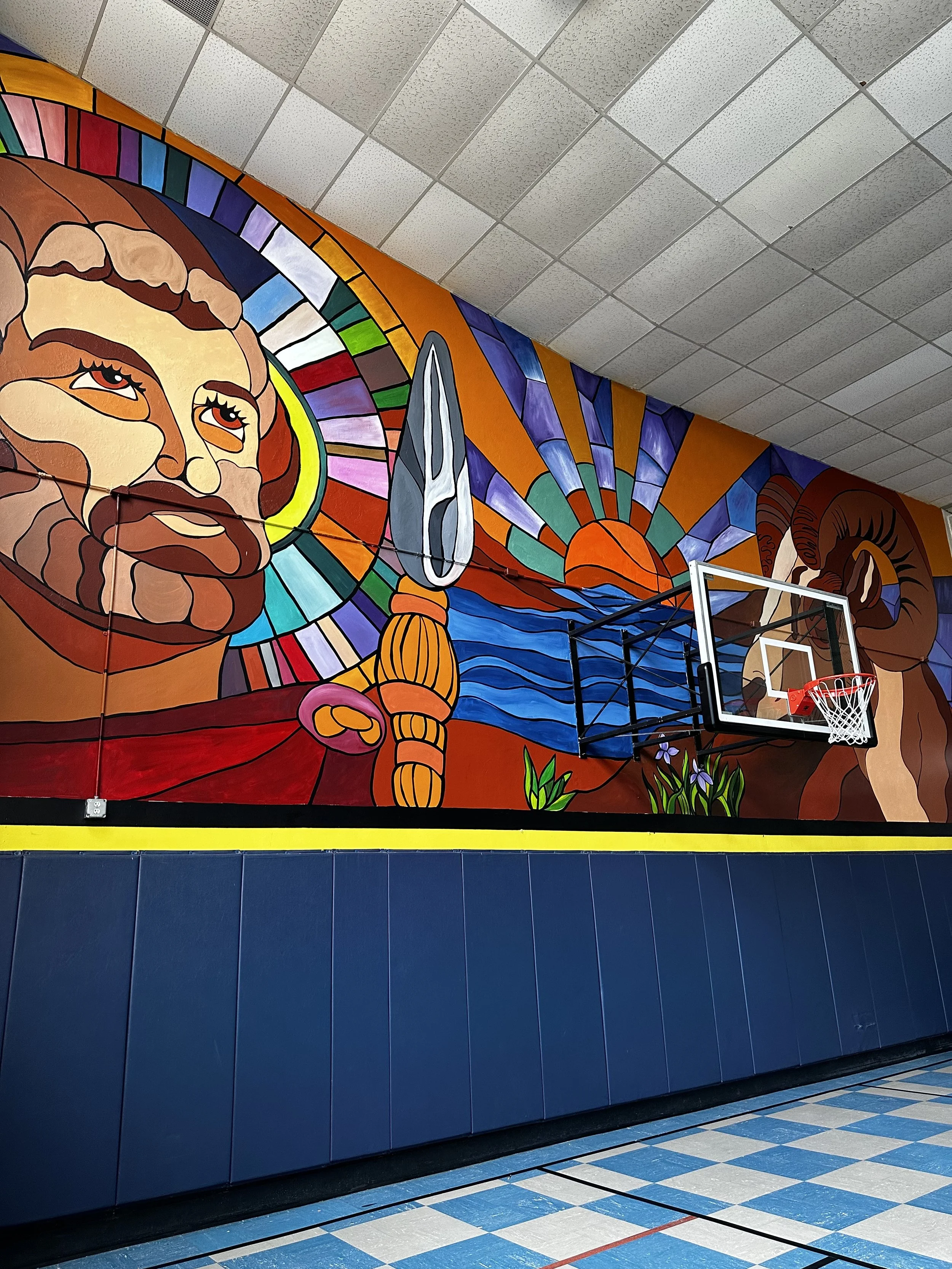 Colorful mural on gym wall depicting a bearded man with a halo, a sunset over water, a ram's horn, and vibrant abstract designs.