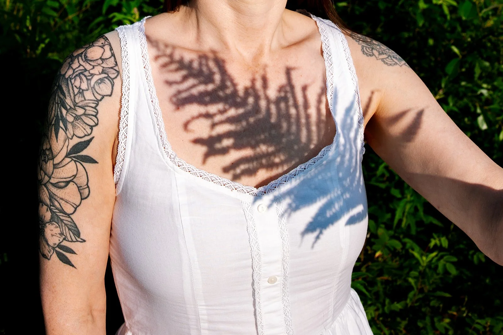 Close-up of a woman in a white dress with the shadow of a fern plant cast on her chest.